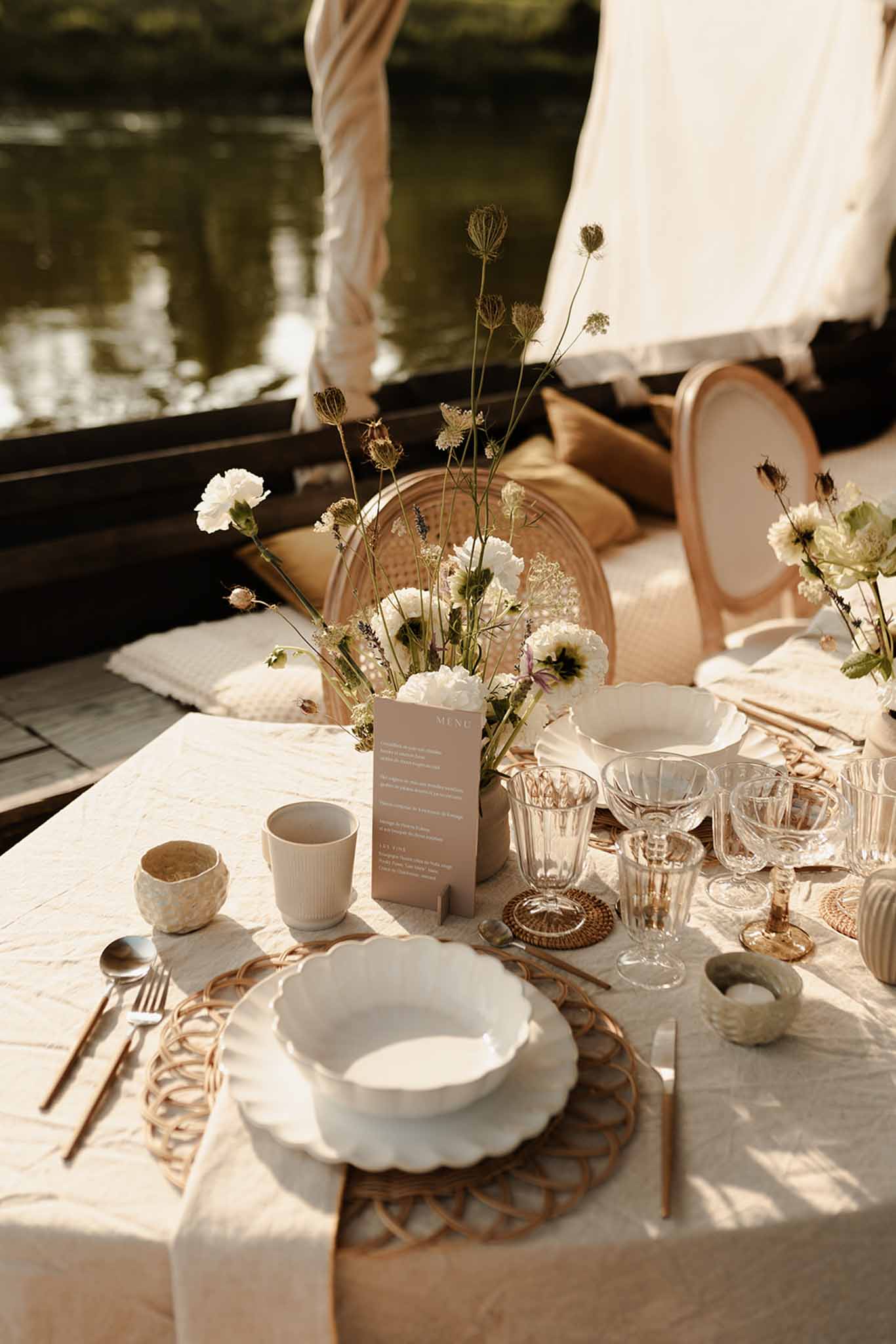 Reception place setting with rattan charger, white carnation centerpiece, brass flatware, and woven accents