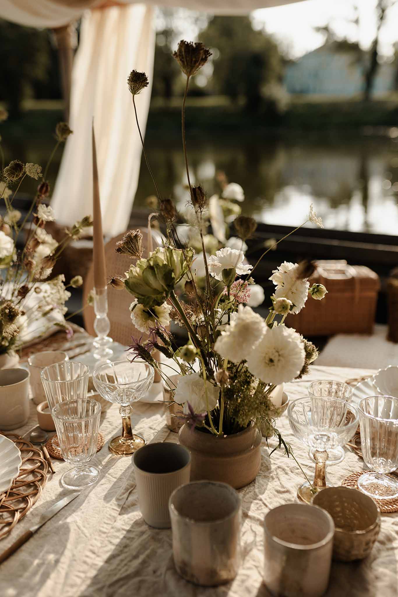 Reception table centerpiece with dried seed pods and white carnations in ceramic vessel on cream linen tablecloth