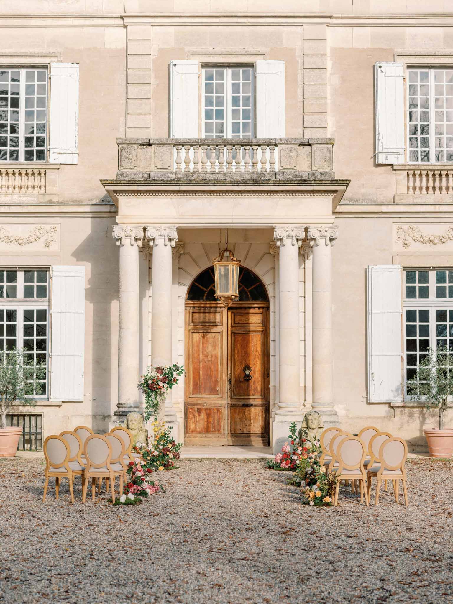Ceremony setup in neoclassical château courtyard with bentwood chairs and coral-blush floral arrangements