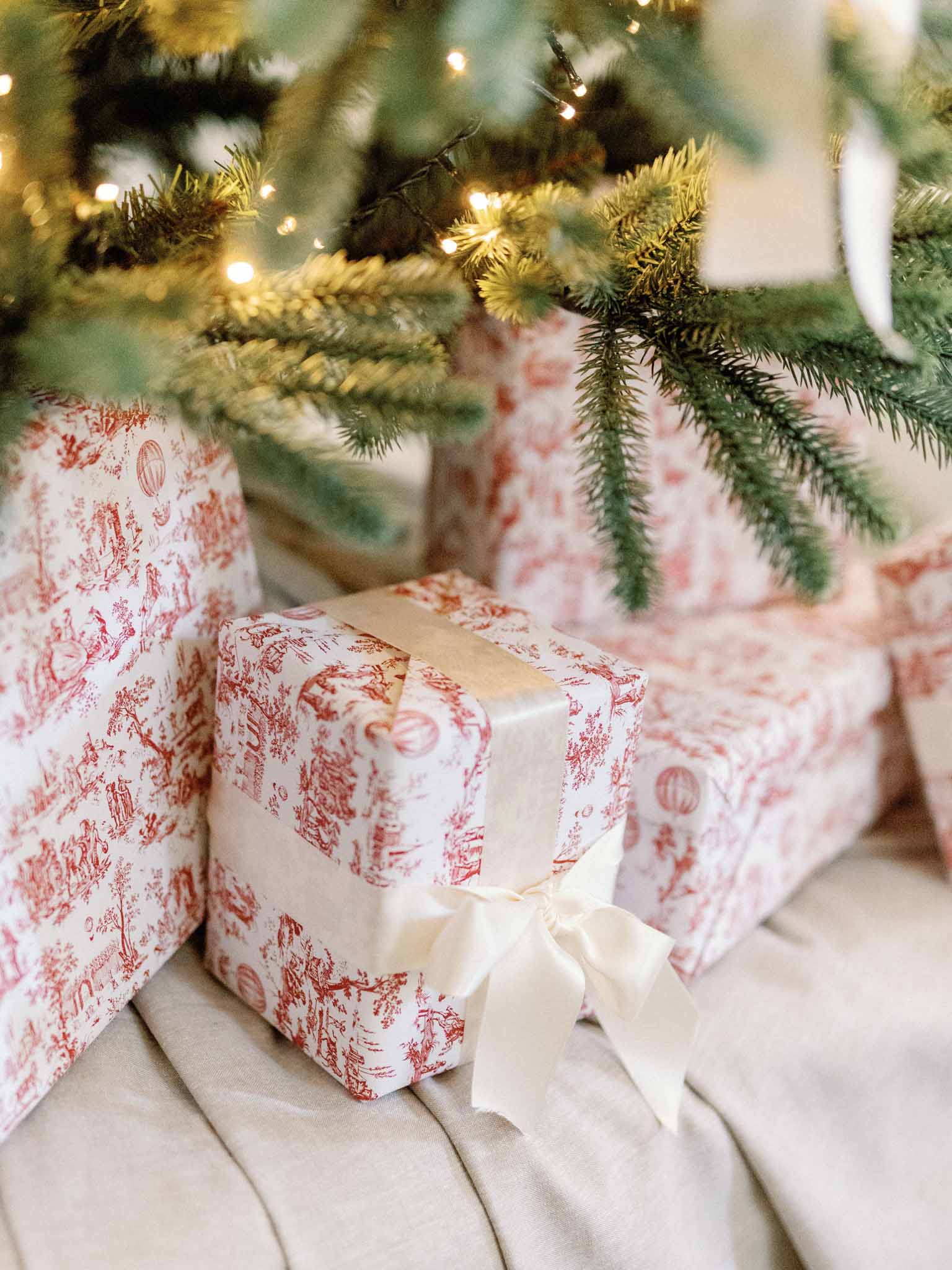 Wedding favors in red and white toile paper with cream ribbons under evergreen garland with fairy lights
