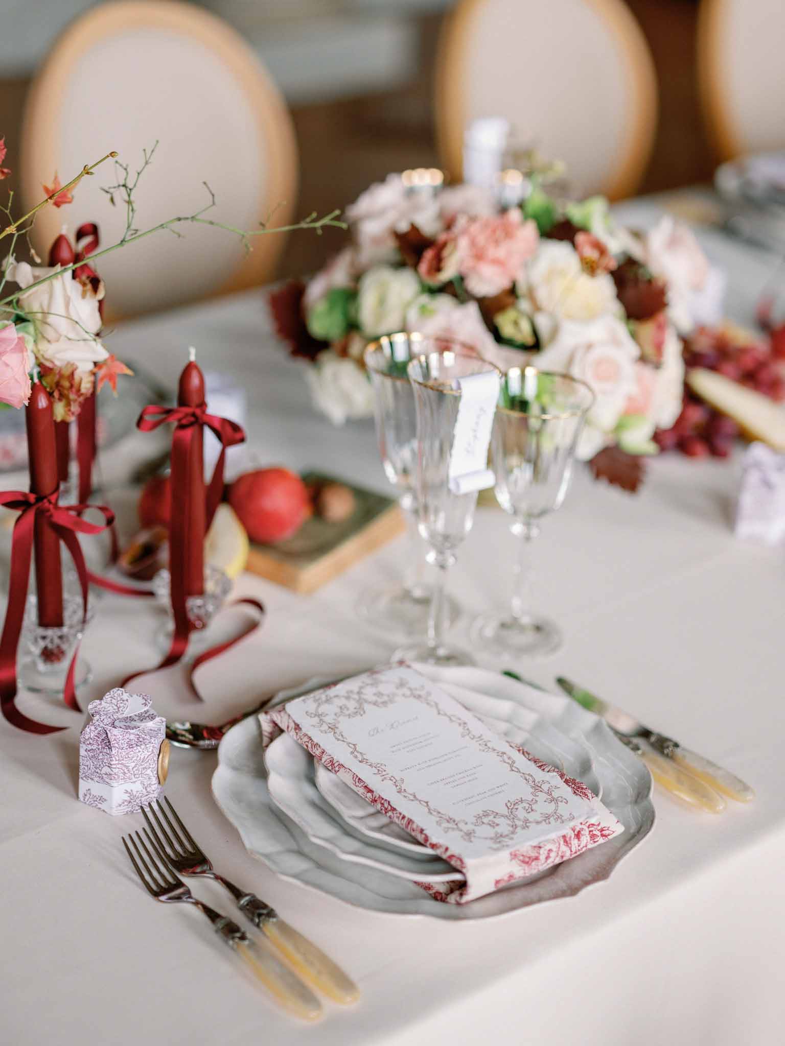 Reception place setting with red napkin, burgundy ribbon candles, and cream and red floral centerpieces