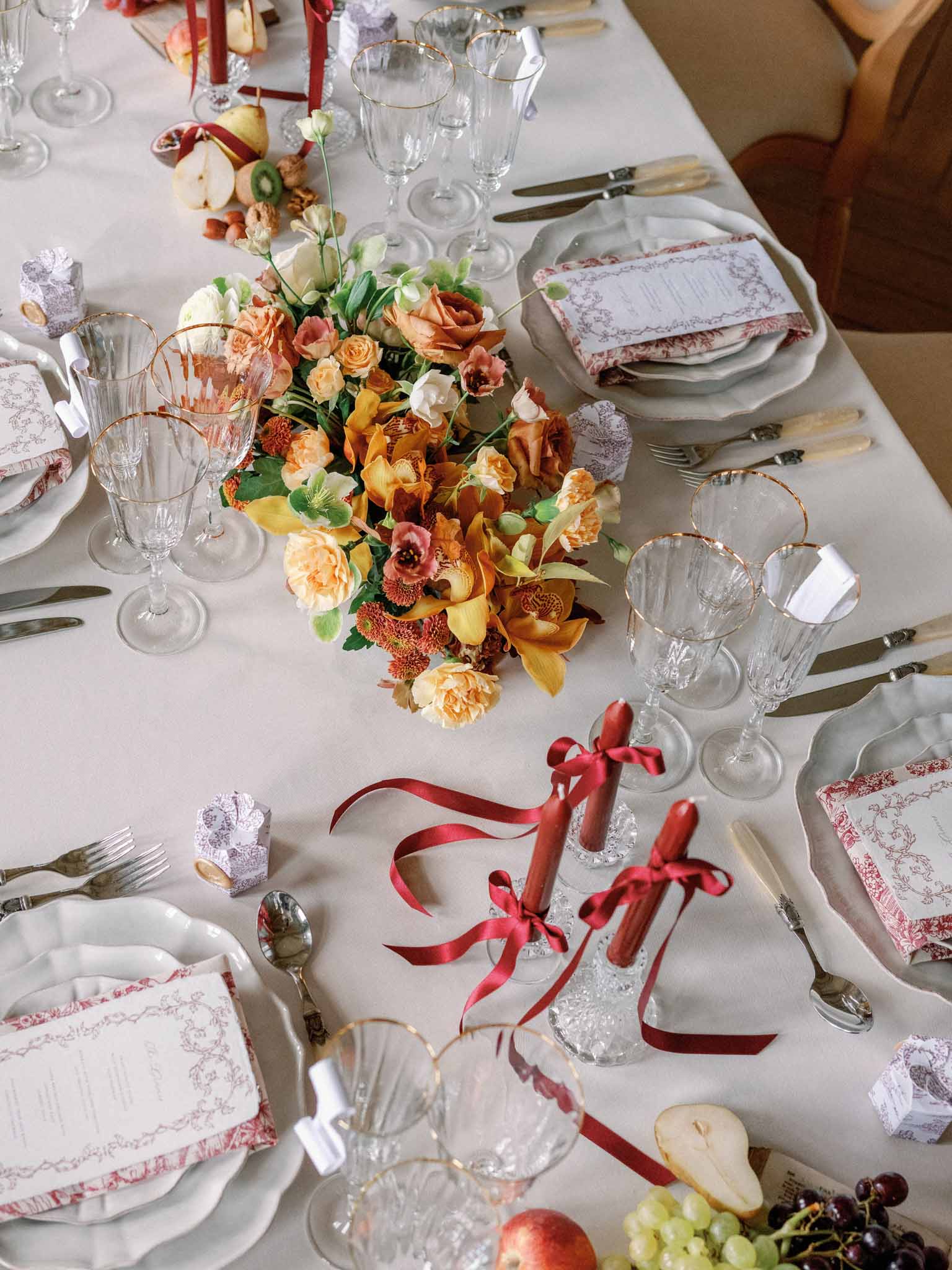 Overhead view of autumn reception table with peach roses, rust dahlias, crimson ribbons, and coordinated place settings