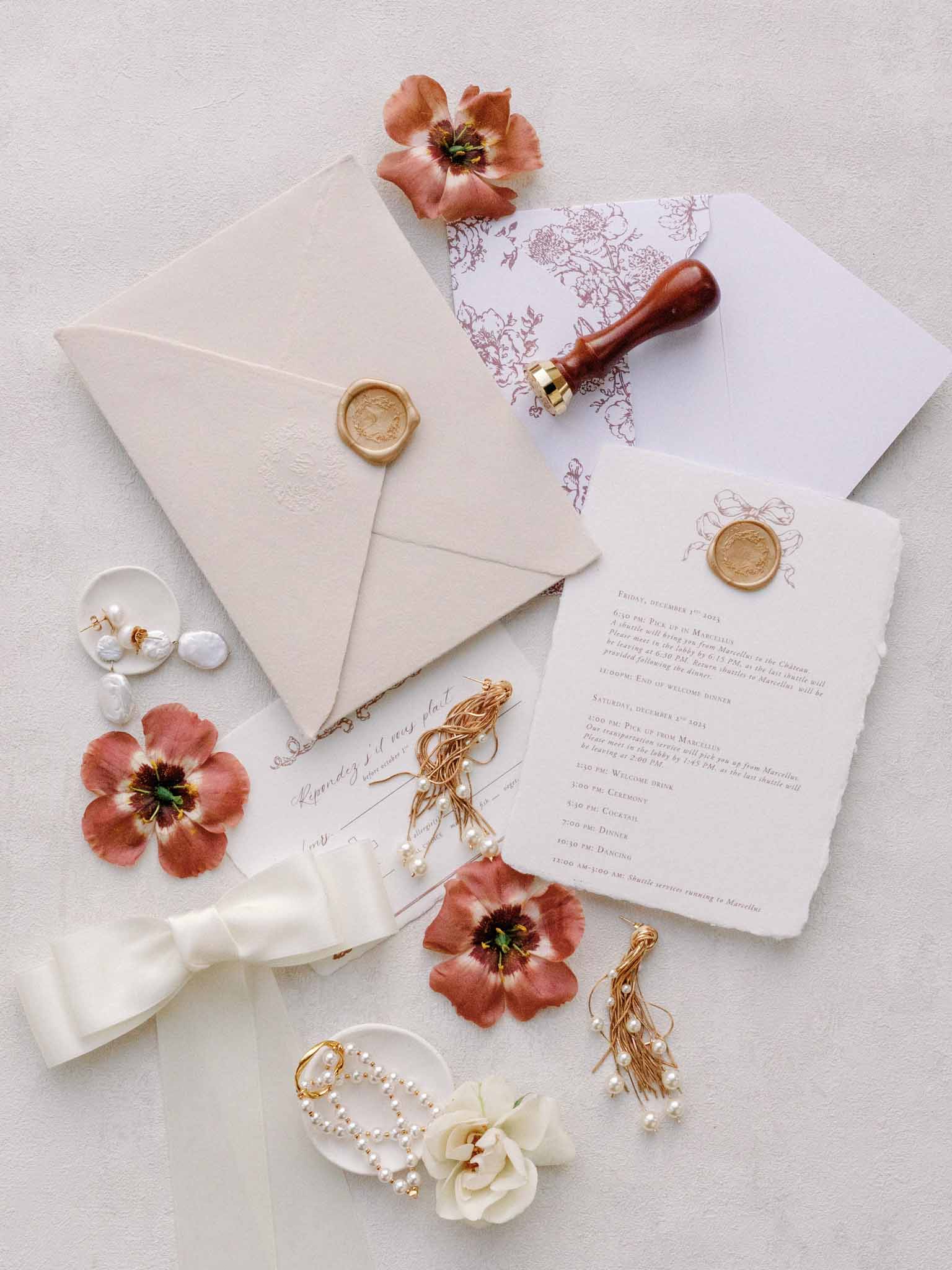 Flat lay of wedding stationery with gold wax seals, terracotta anemones, pearl jewelry, and silk ribbon
