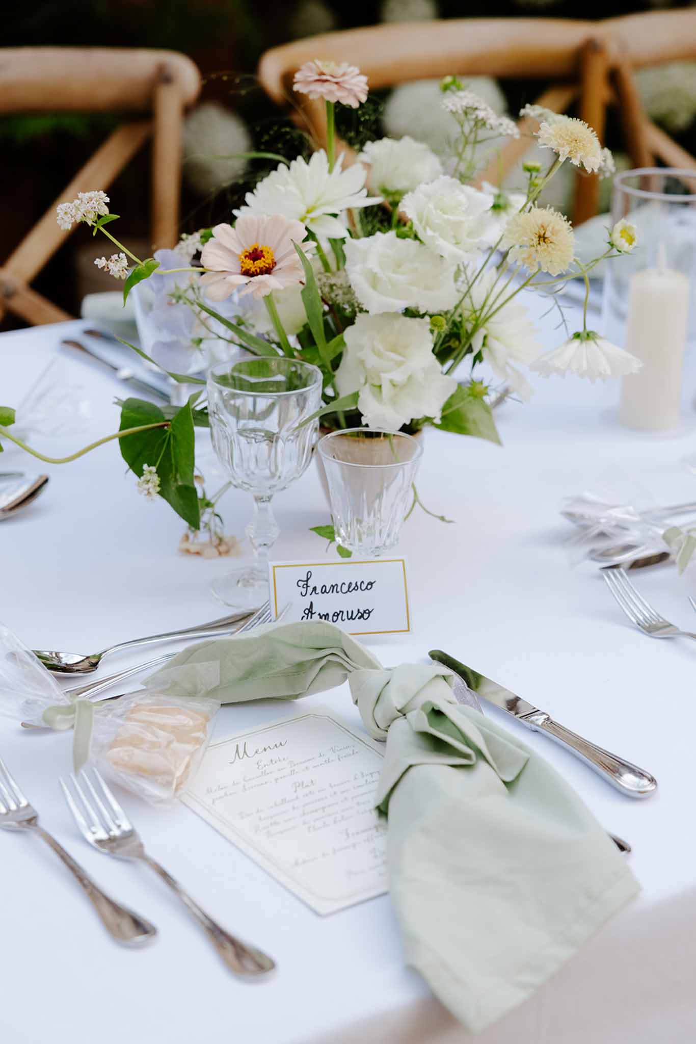 Reception table place setting with sage linen napkin, handwritten place card, white roses and gerbera daisies centerpiece