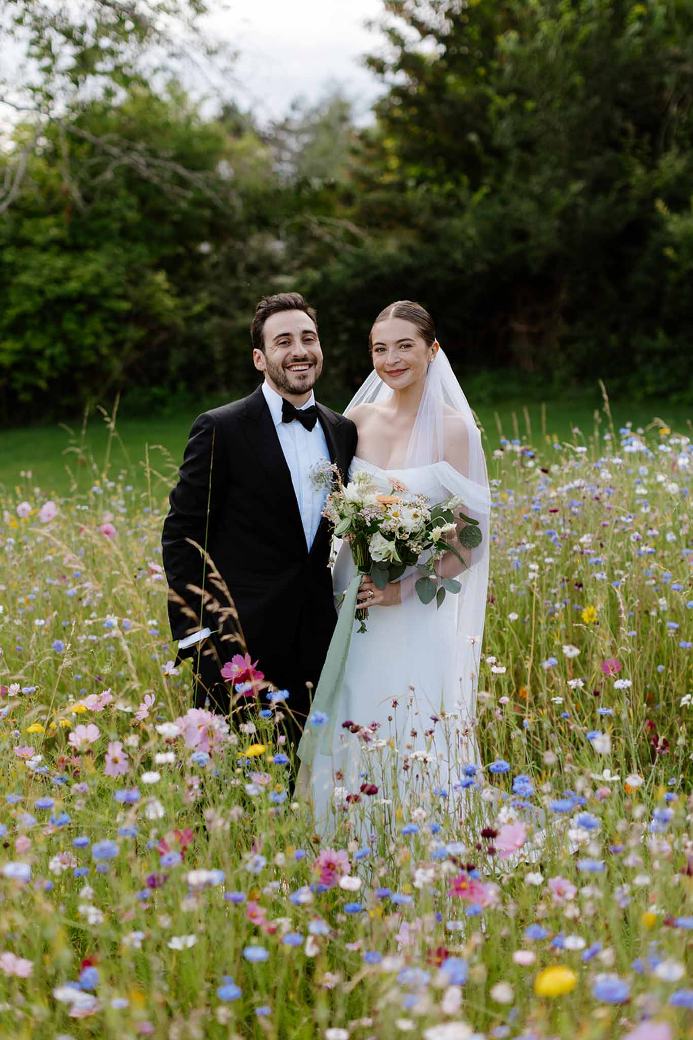 Bride and groom posing together in a wildflower meadow with colourful blooms