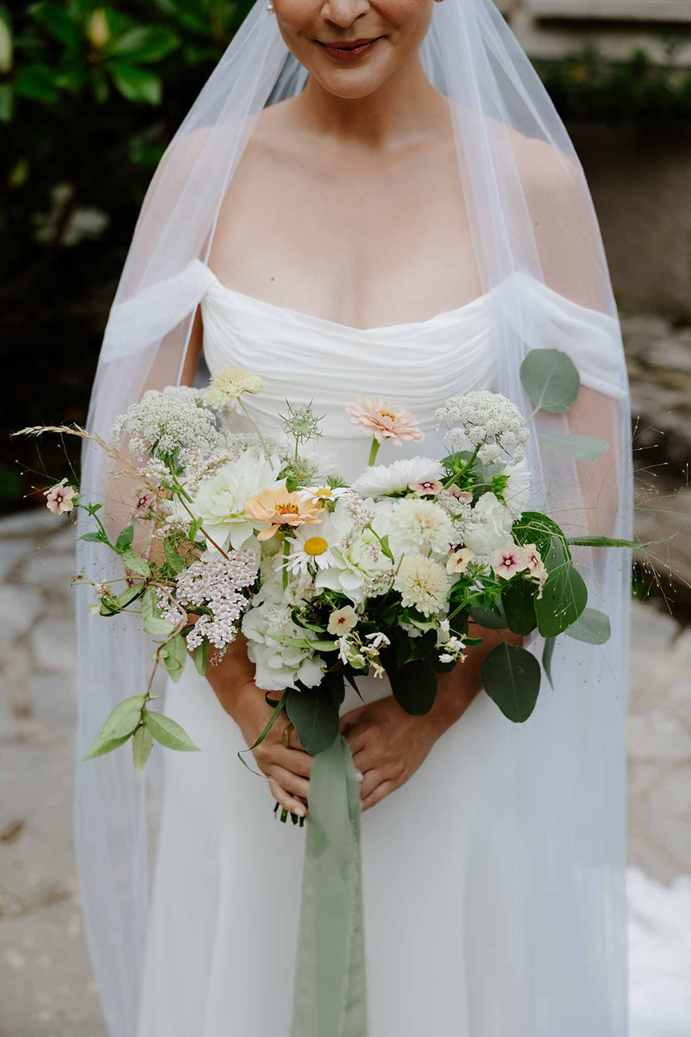 Bride in ivory silk cowl-neck gown holding loose garden bouquet of cream dahlias, sweet peas, and trailing eucalyptus