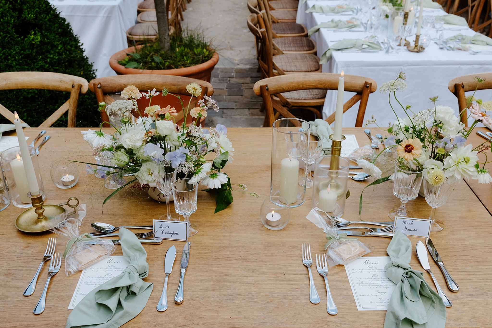 Reception table detail with white daisies, baby's breath, sage napkins, brass candle holders, and cross-back chairs