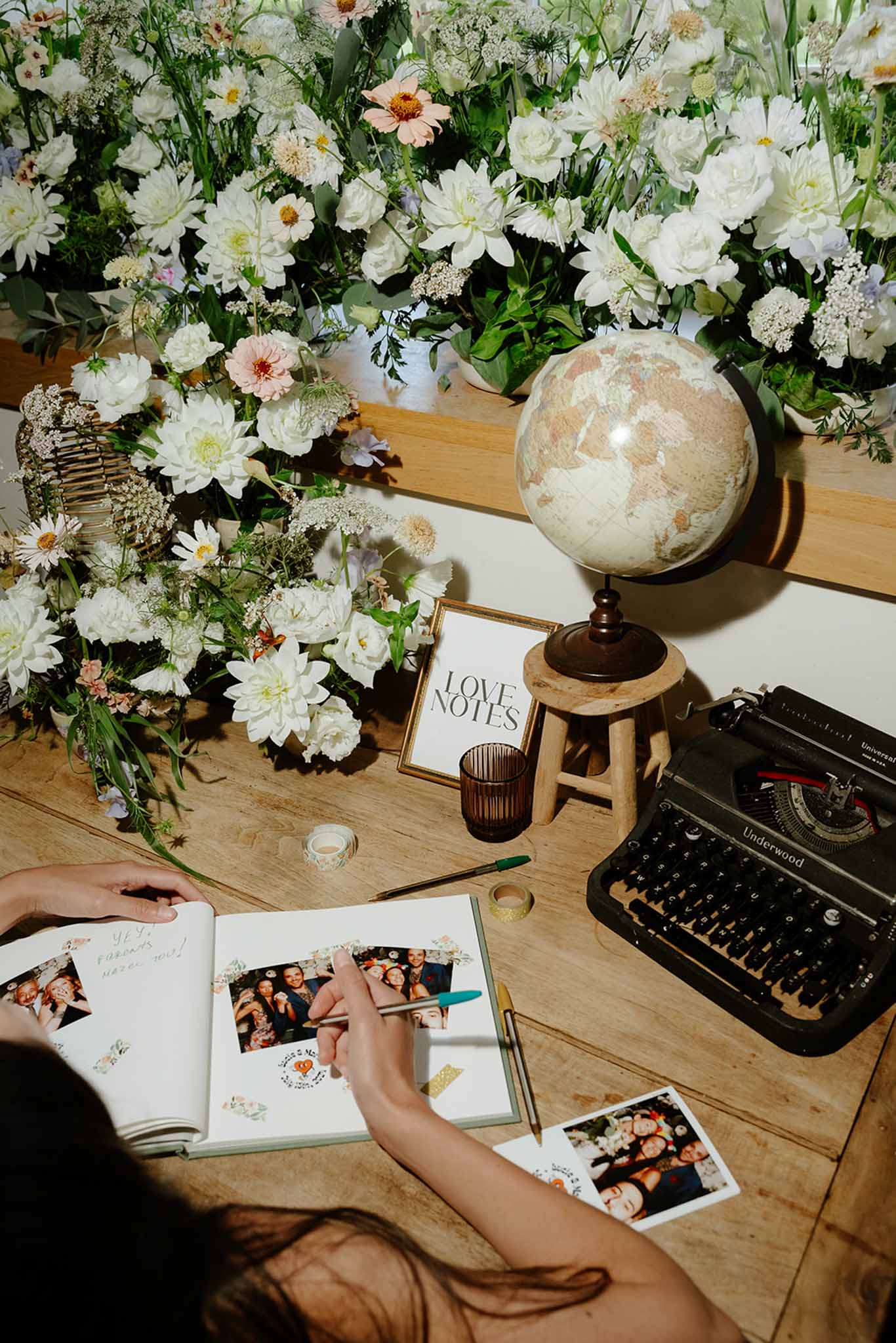 Guest signing white guest book at wooden table with abundant white floral arrangement and vintage black typewriter as decor