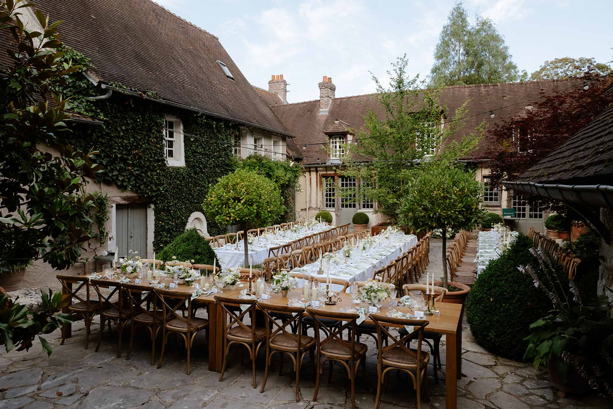 Courtyard reception with long tables, white hydrangea centerpieces, and ivy-covered stone manor