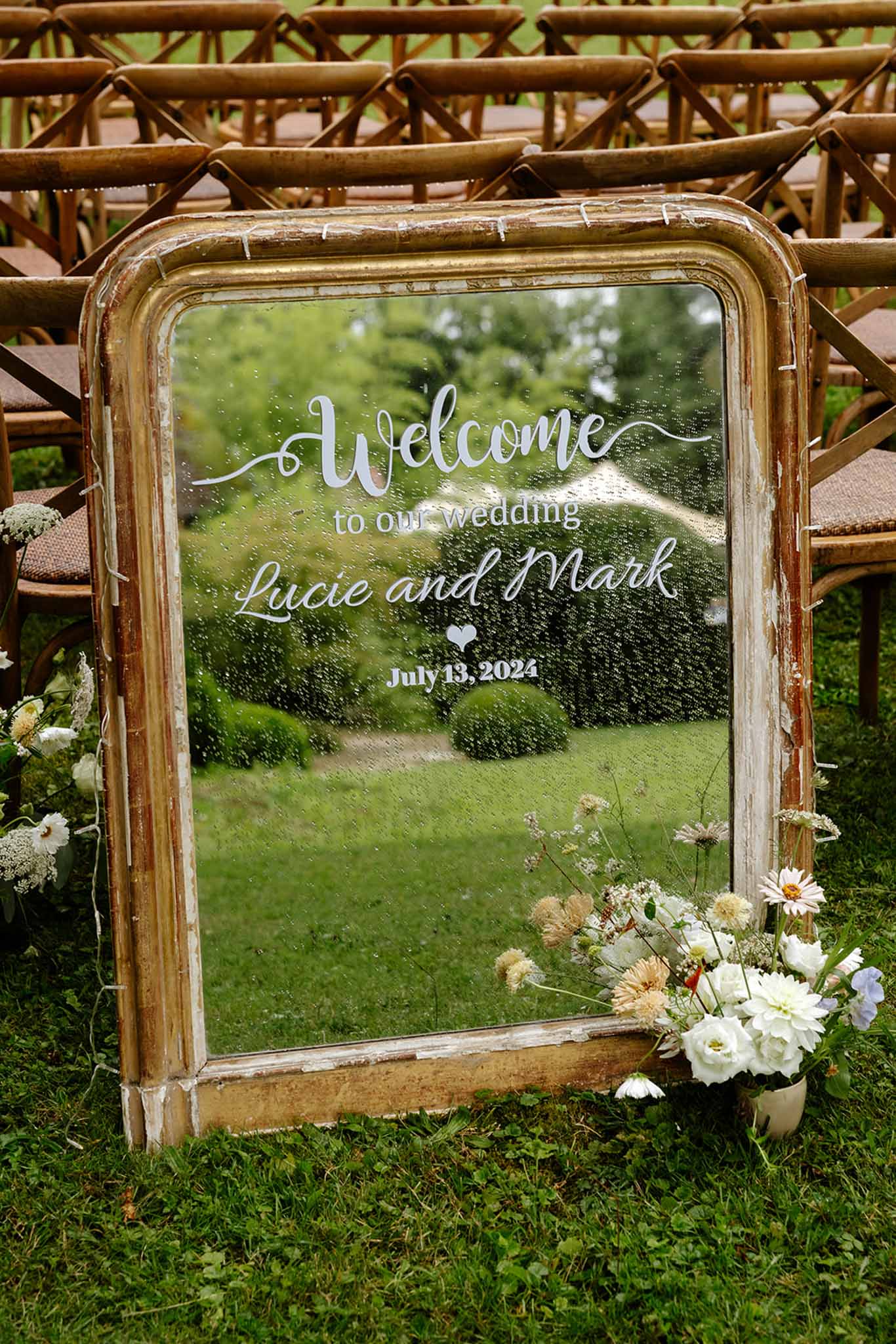 Vintage gold-framed mirror welcome sign with calligraphy and white rose arrangement in a garden ceremony setting