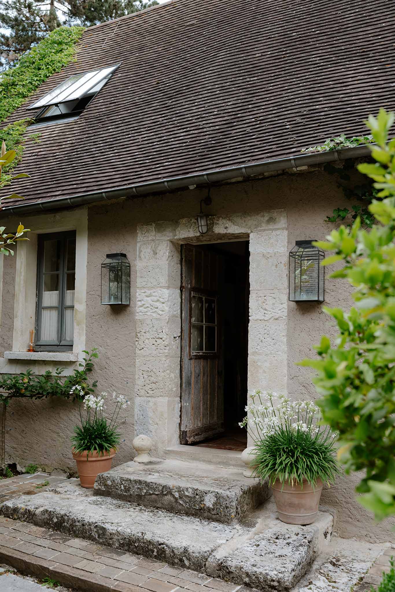 Exterior of rural stone cottage venue with dark tile roof, climbing ivy, and white flowering planters