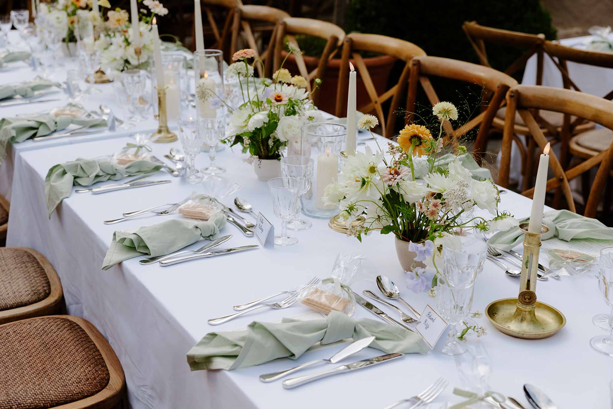 Reception table with white peony centerpieces, sage green napkins, brass candlesticks, and cross-back chairs