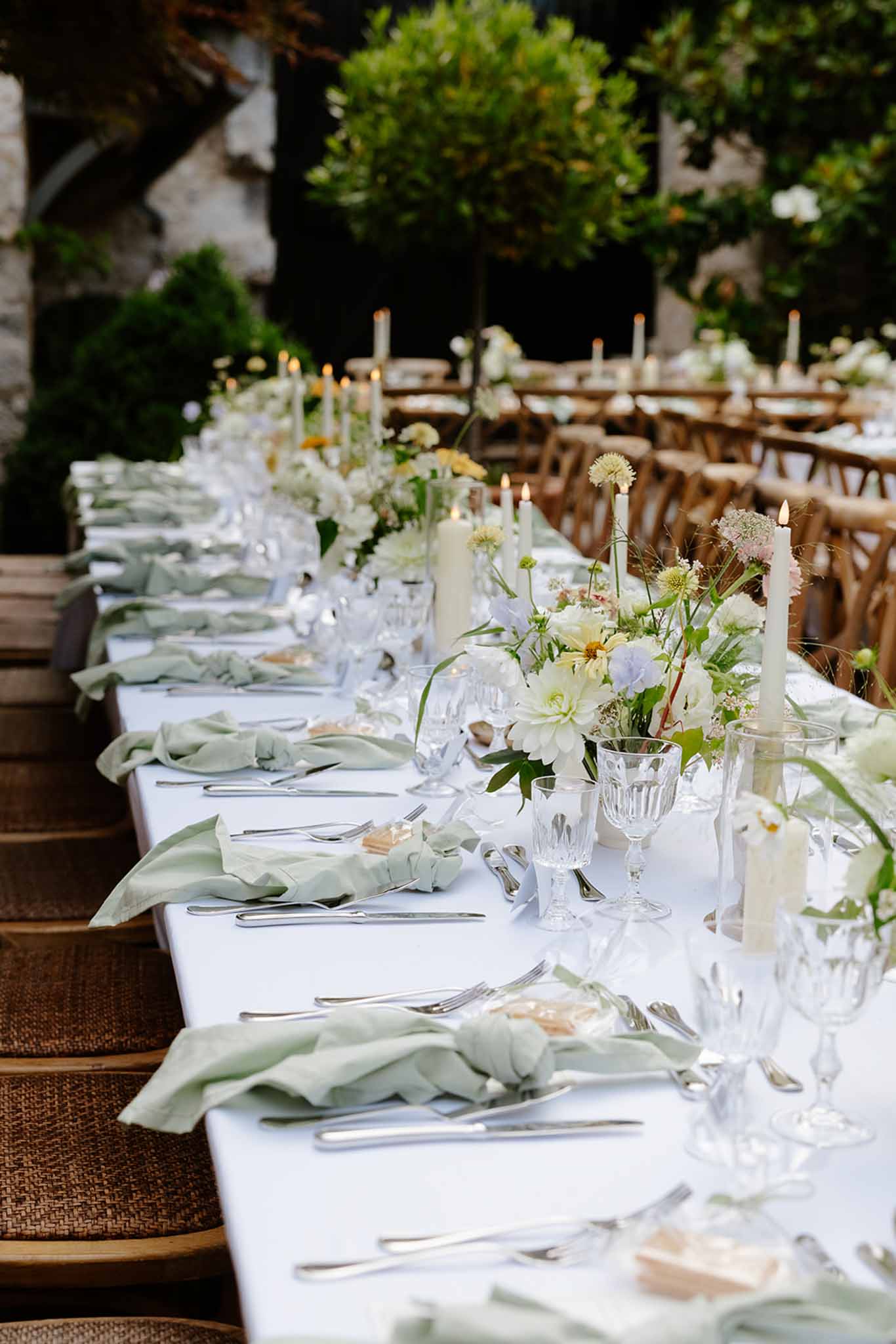 Reception table with sage green napkins, white dahlia centerpieces, and taper candles