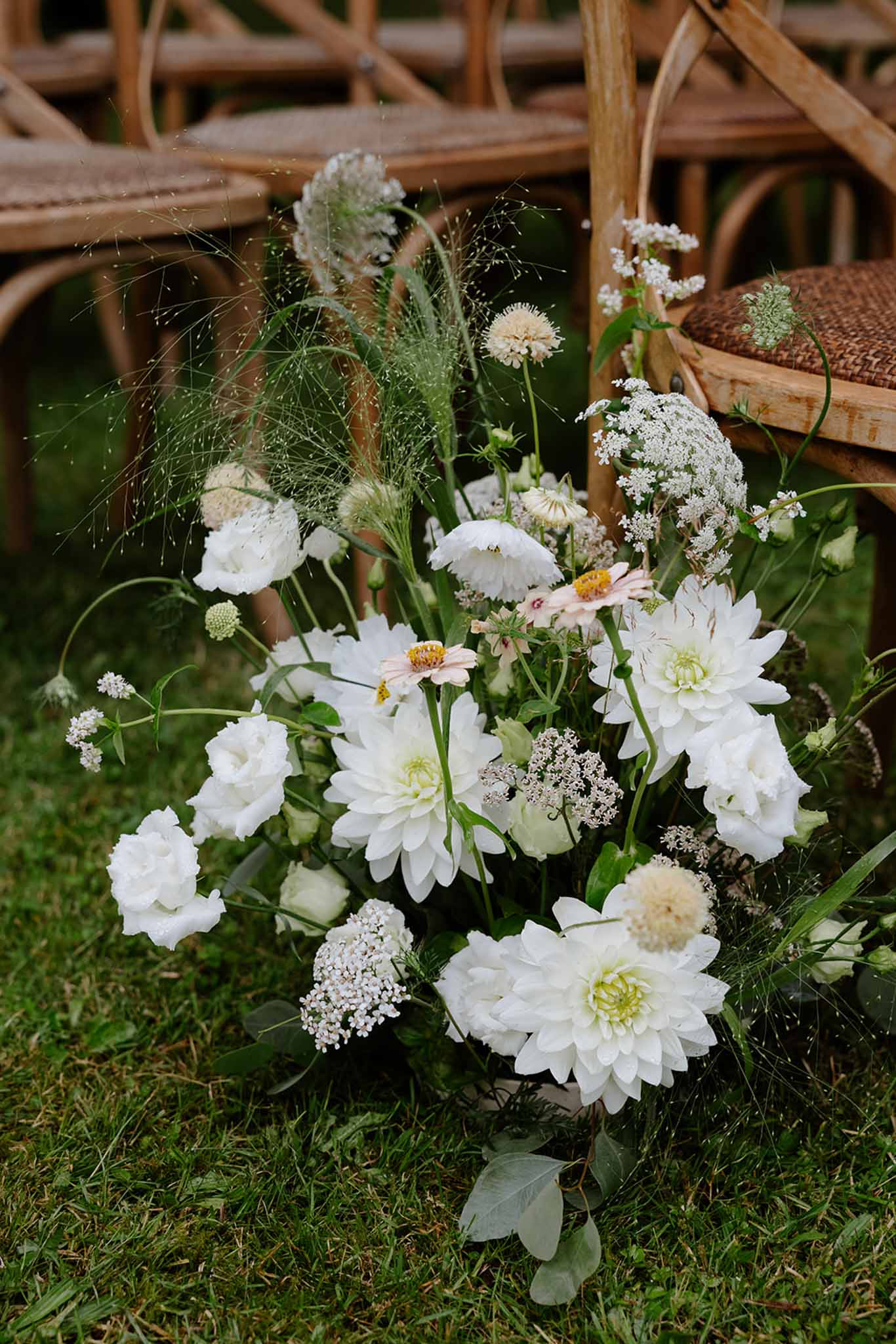 White dahlias, Queen Anne's lace, dusty miller, and ornamental grass ceremony arrangement in burlap container on grass