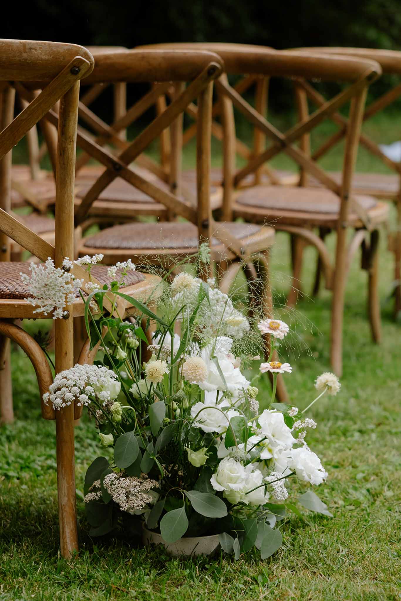 Wooden cross-back ceremony chair with white rose and baby's breath floral arrangement tied to frame