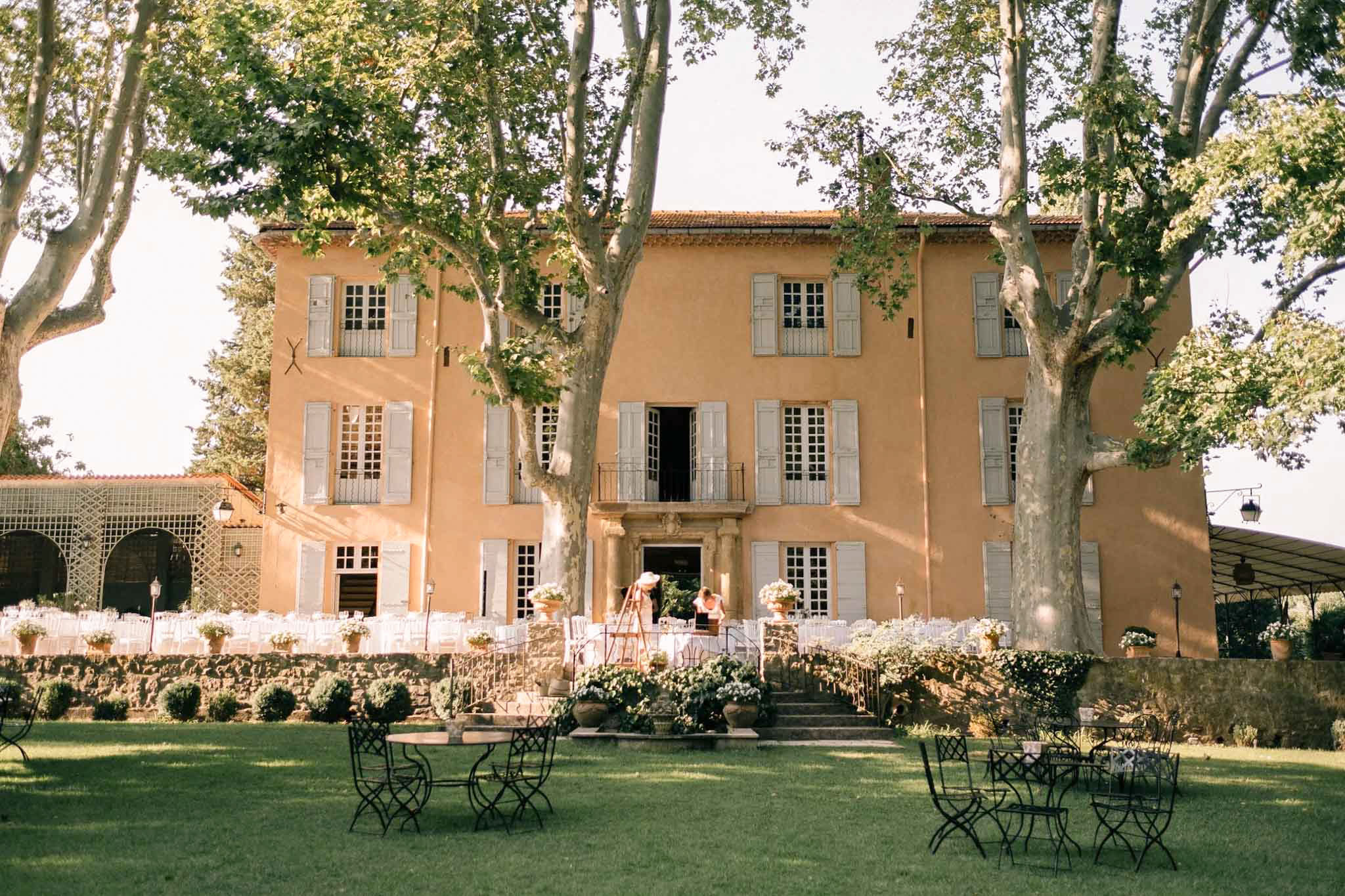 Ochre Provencal bastide with blue shutters and white ceremony chairs arranged on the front terrace
