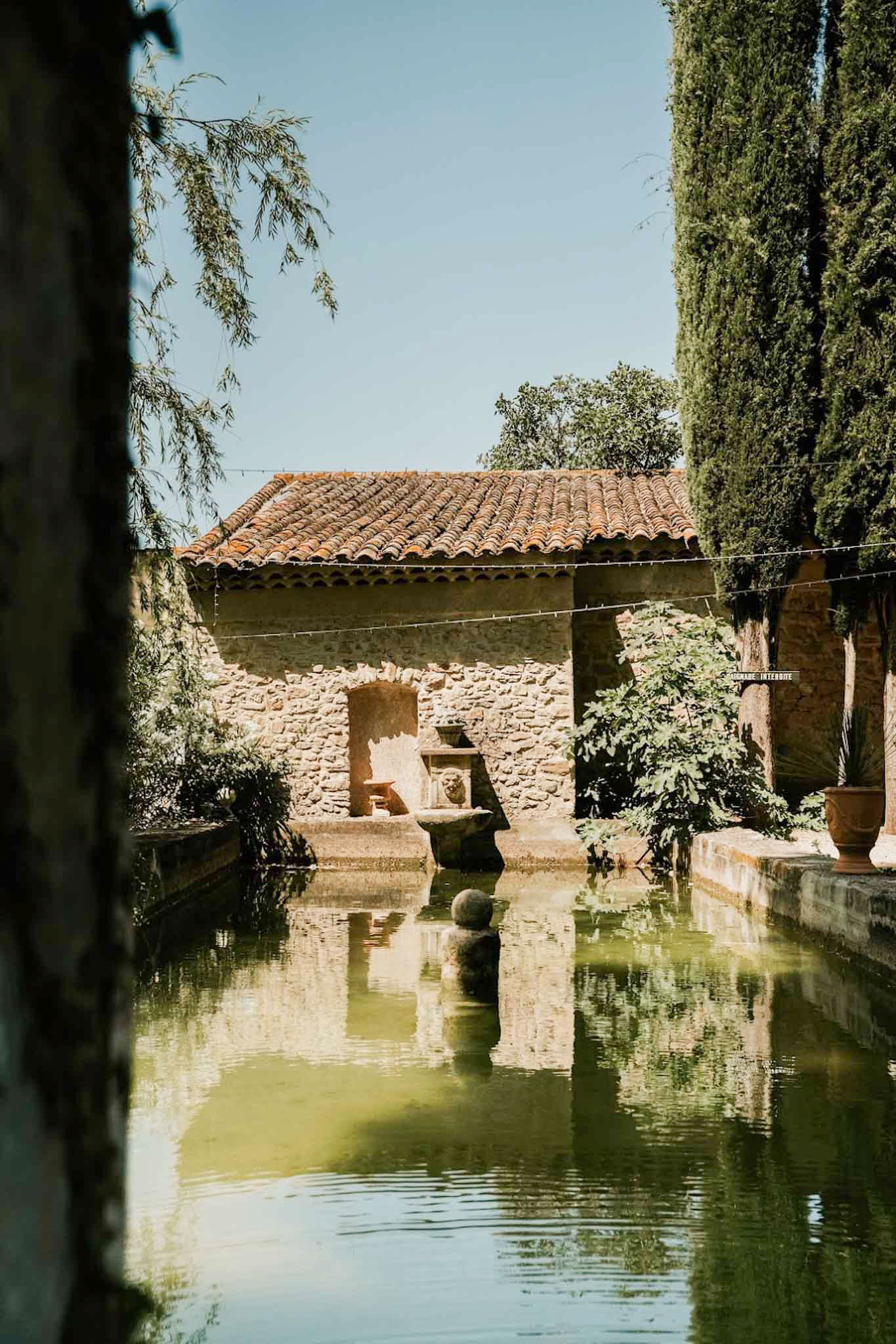 Rectangular ornamental pool reflecting Provencal stone building with lion fountain and fairy lights