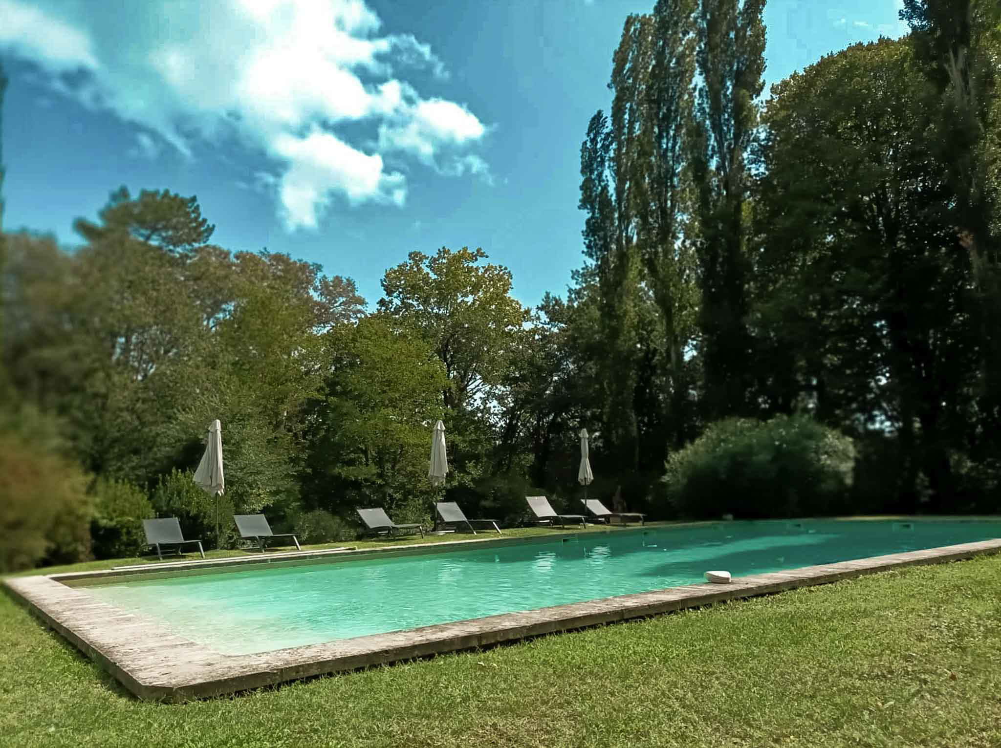 Rectangular turquoise pool with grey sun loungers and closed white parasols at French estate venue
