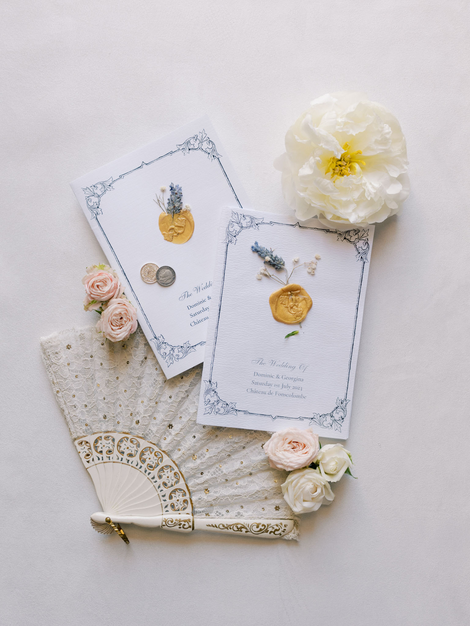 Wedding stationery flat lay with pressed flowers, gold wax seals, lace, and peach roses
