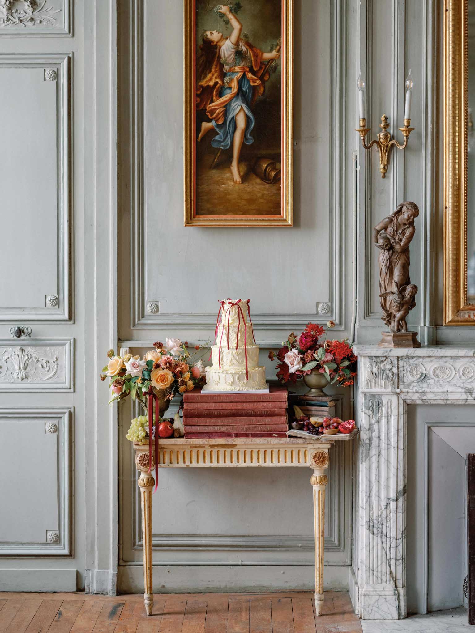 Ivory wedding cake with coral ribbon on gilded console table in classical salon with pale blue paneled walls