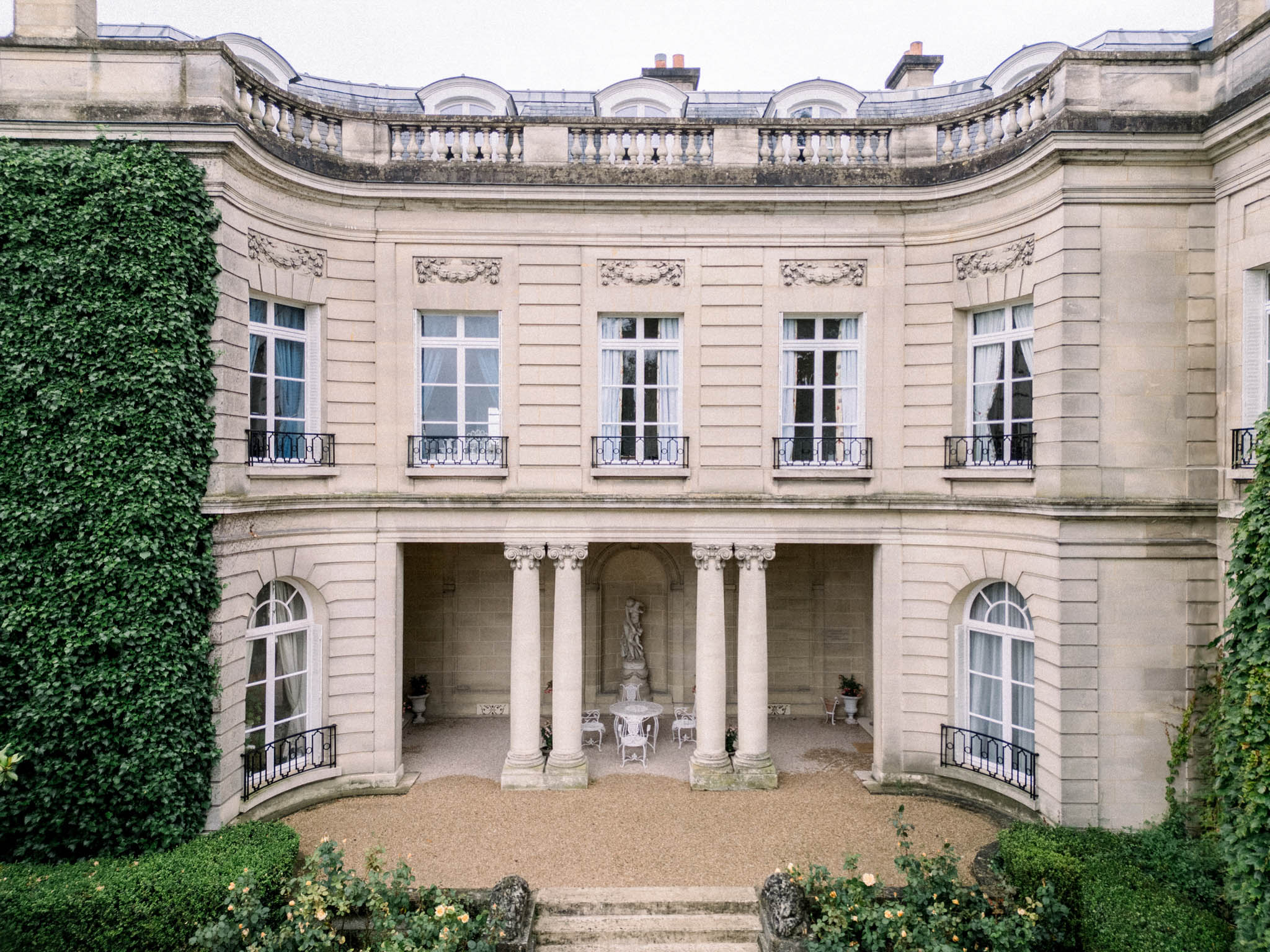 Neoclassical French mansion facade with Ionic columns, wrought-iron balconies, and gravel forecourt