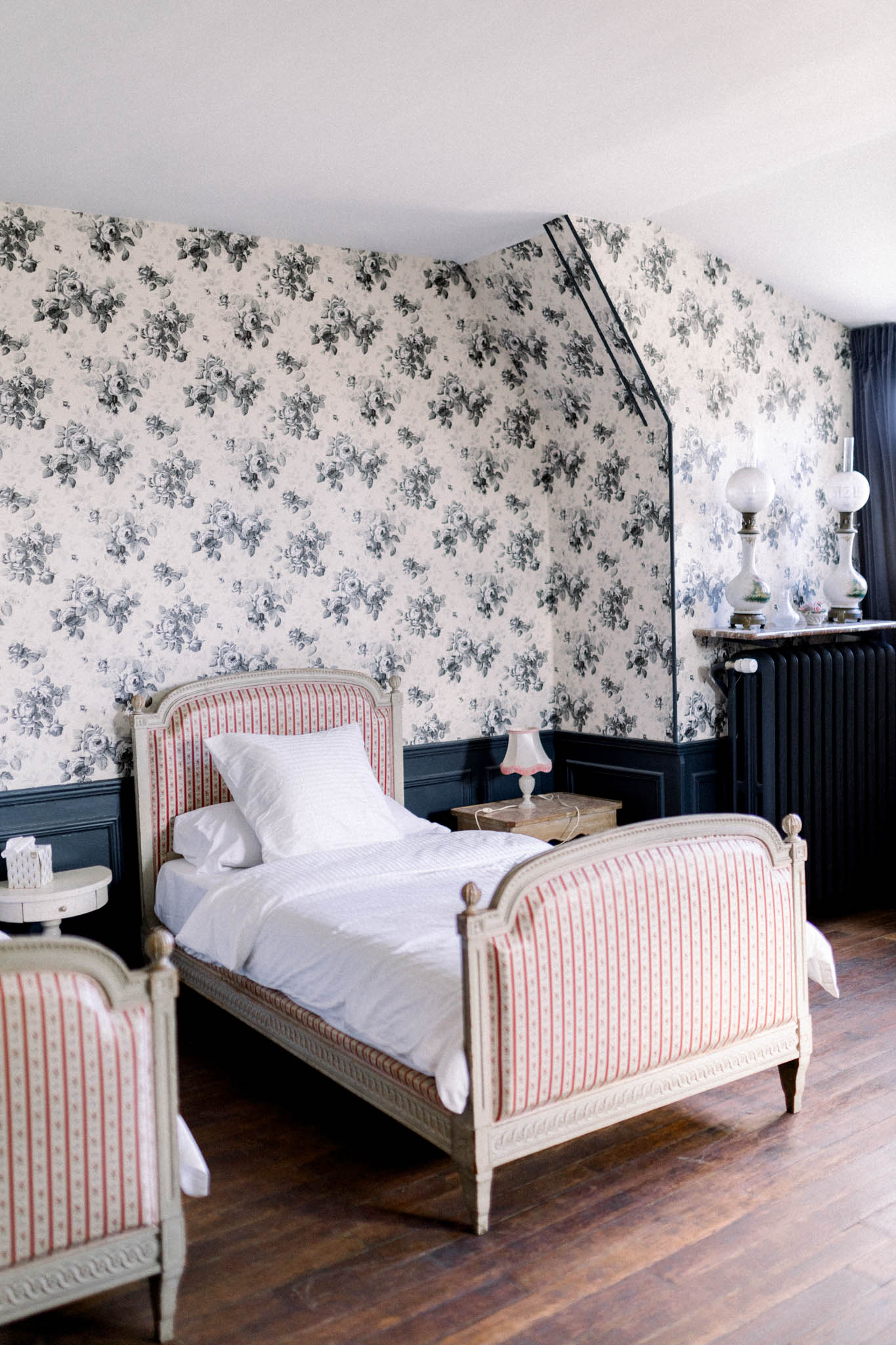 Classic French chateau bedroom with Louis XVI bed, rose-patterned wallpaper, navy wainscoting, and period furnishings