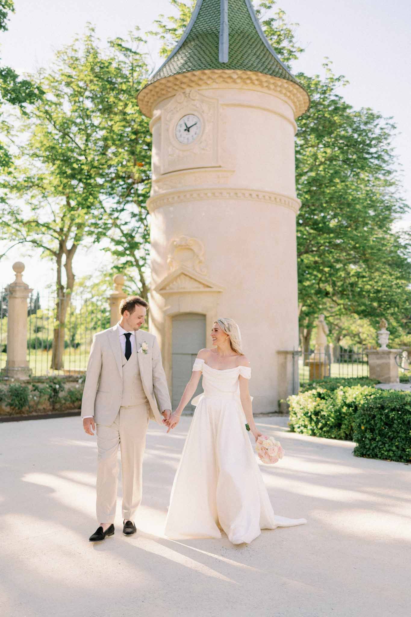 Bride and groom walking holding hands with castle in background by G Dominic and M Marechal