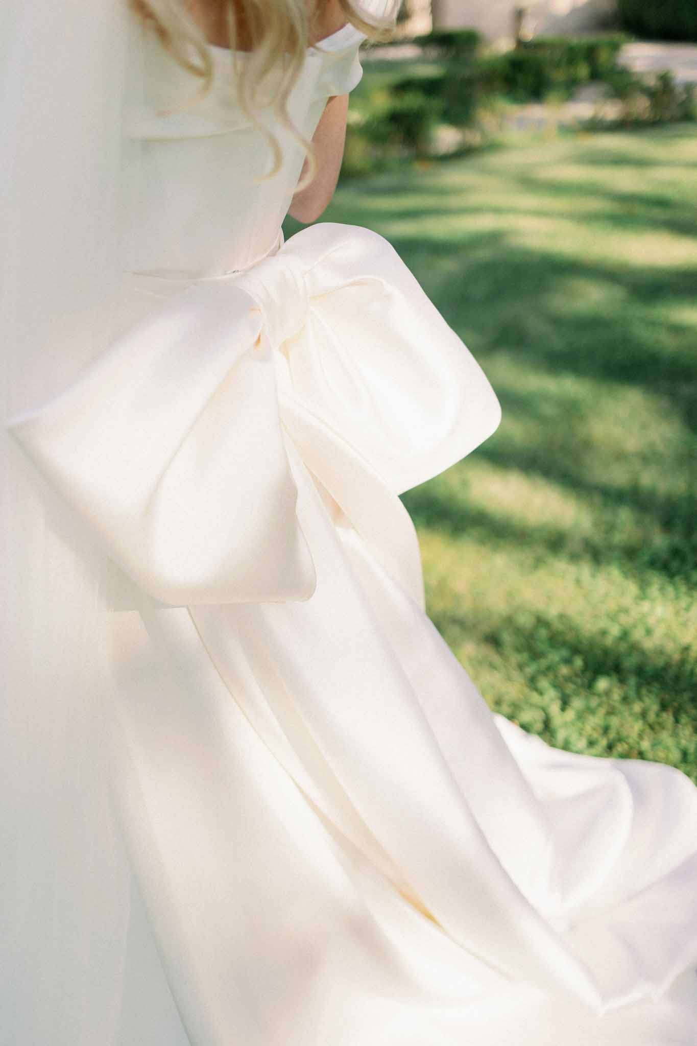 Close-up of bride holding flowing ivory silk wedding dress fabric in an outdoor garden setting