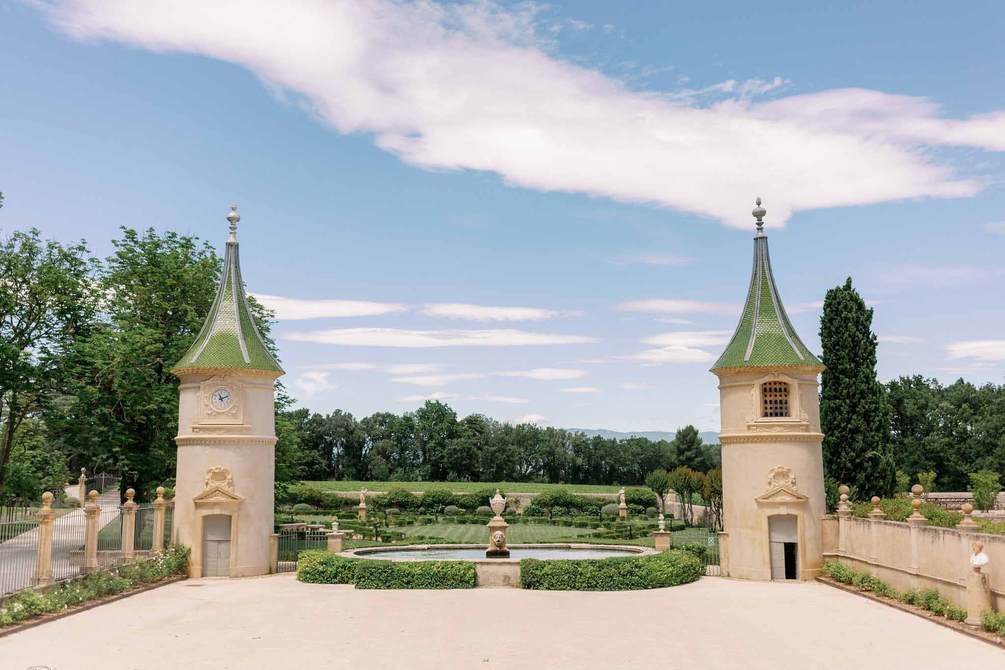 French chateau with two cream stone towers with conical green roofs, central fountain, ornamental urns, vineyard views