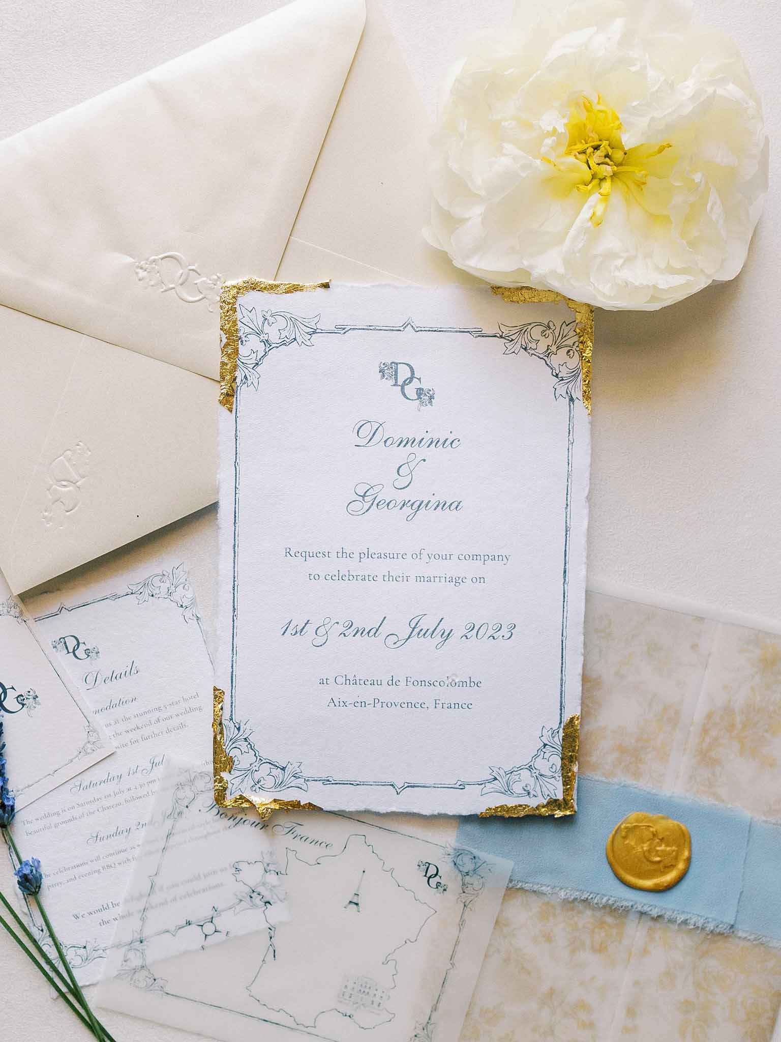 Wedding invitation flat lay for Dominic and Georgina at Château de Fonscolombe, blue script on white card with gold leaf edge