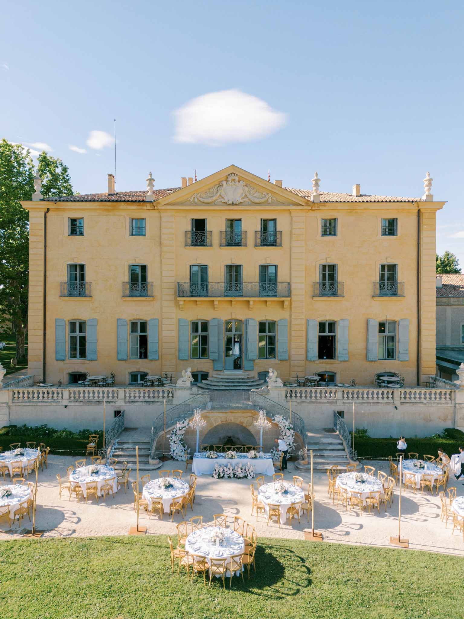 Aerial view of chateau reception terrace, round tables with gold Chiavari chairs, white floral altar, clear tent structures