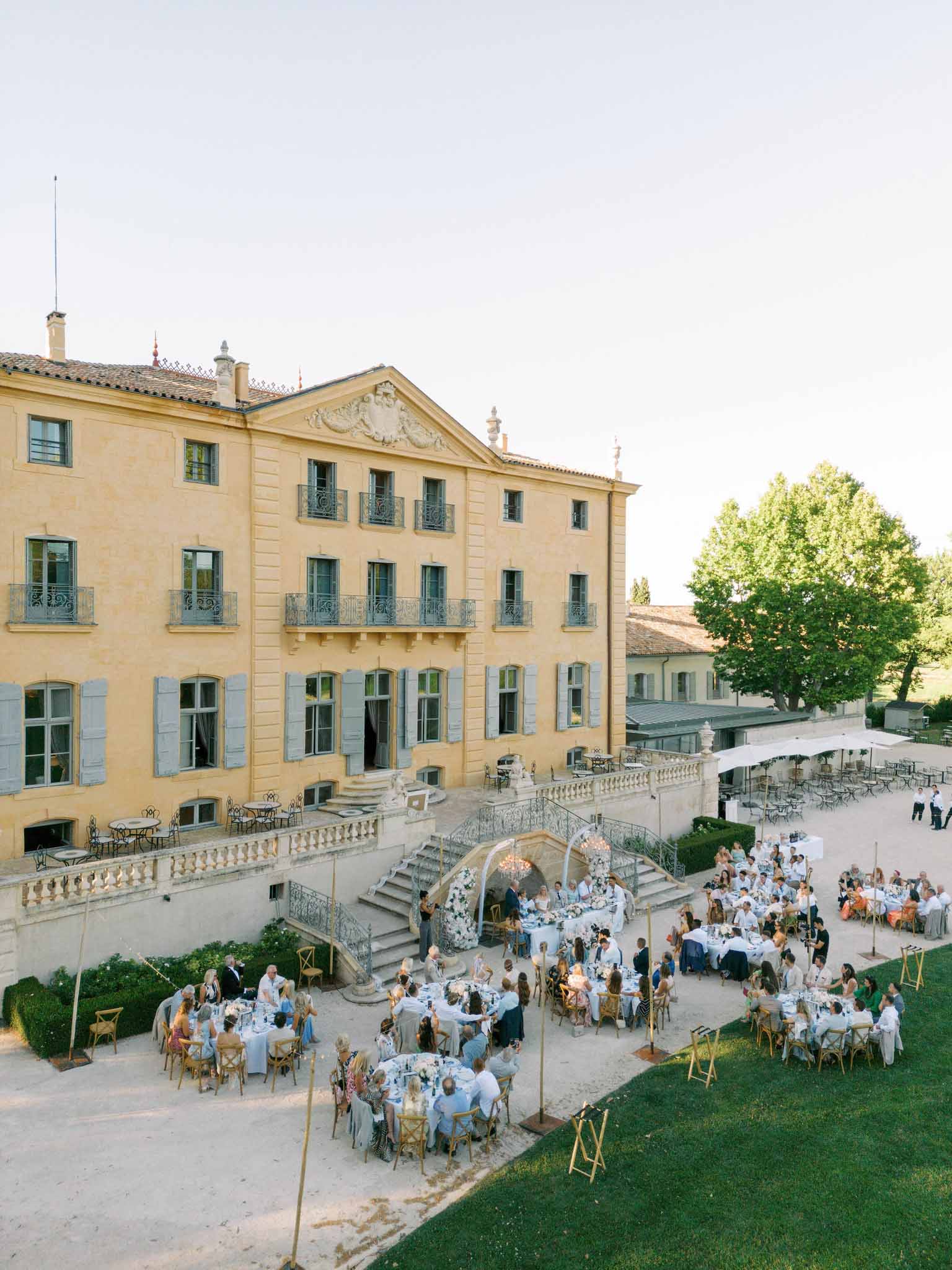 Aerial view of reception at French chateau, 150-200 guests at round tables with pale blue linens, arched floral installation