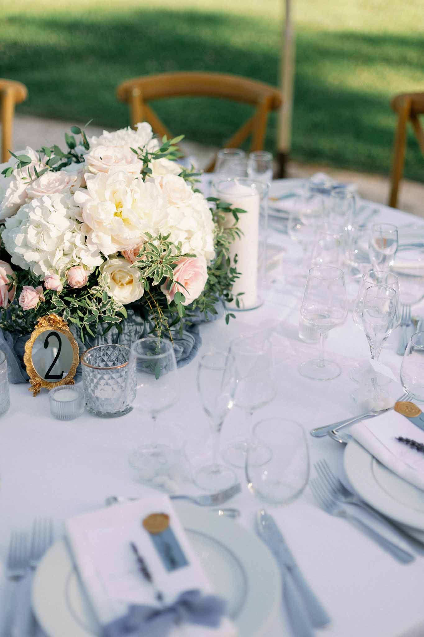 Reception table detail with white and blush peony centerpiece, gold table number, and cross-back chairs
