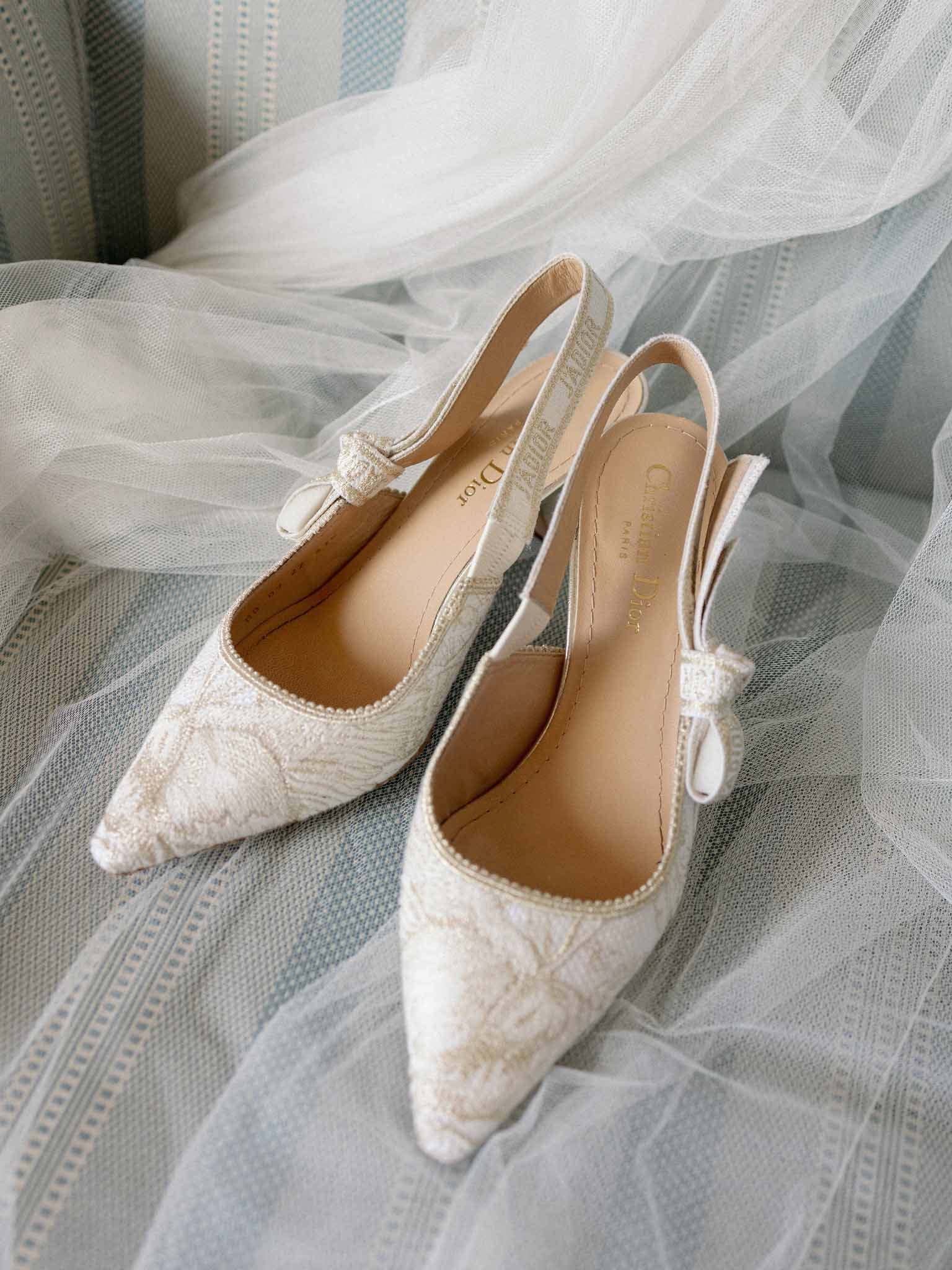 Ivory lace slingback bridal heels with ribbon bows displayed on tulle and pale blue fabric
