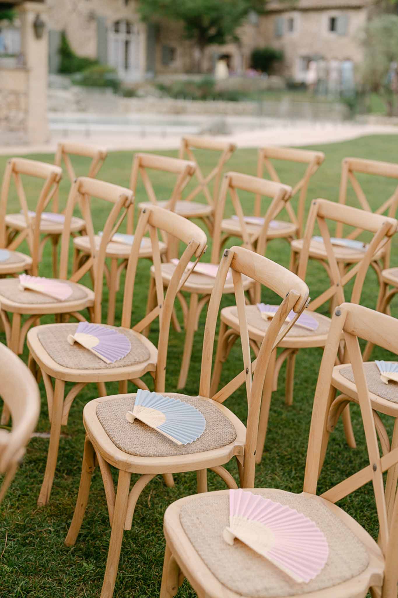 Ceremony chairs with pastel paper fans in pink, lavender, and cream on stone villa lawn