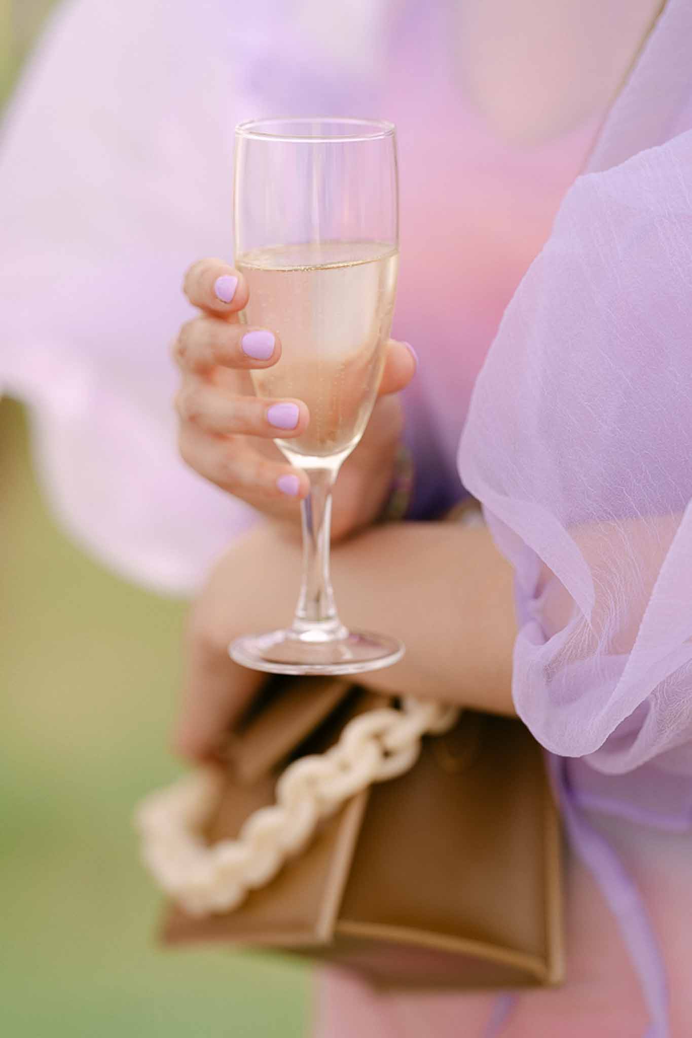 Close-up of hand holding champagne flute with pearl bracelet and lavender tulle dress
