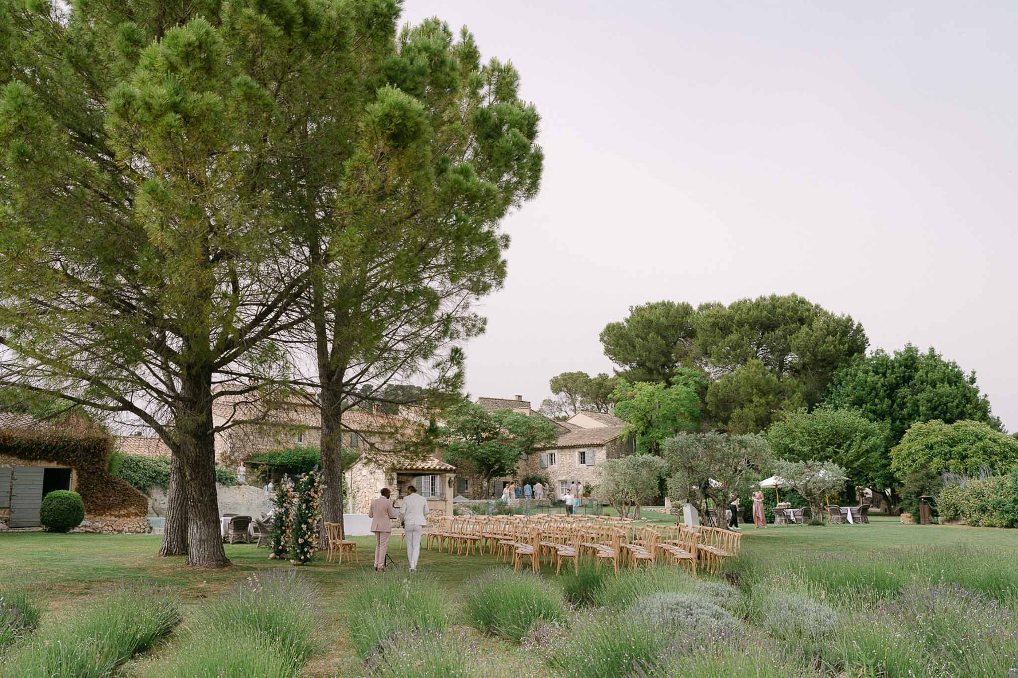 Outdoor ceremony setup in a Mediterranean garden with wooden bistro chairs and stone buildings