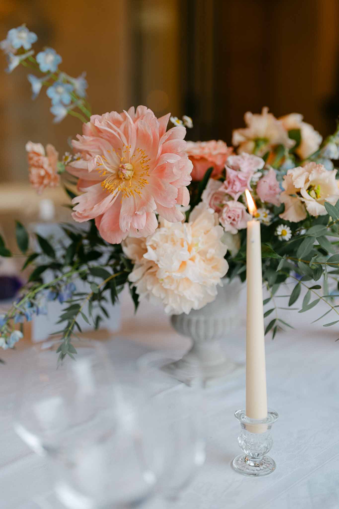 Wedding table centerpiece with coral peonies, cream ranunculus, and blue forget-me-nots in white ribbed vase
