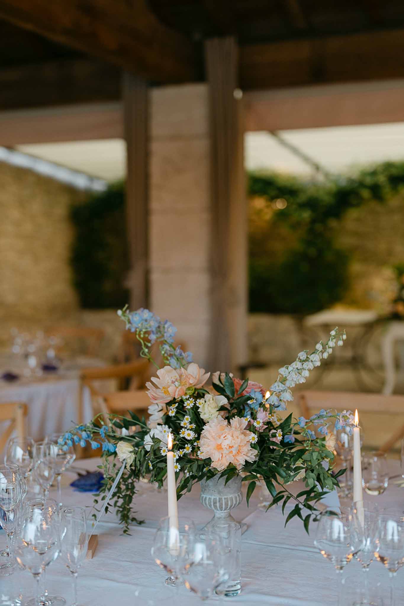 Reception table centerpiece with peach dahlias, blue delphiniums, and eucalyptus in ribbed glass vase outdoors