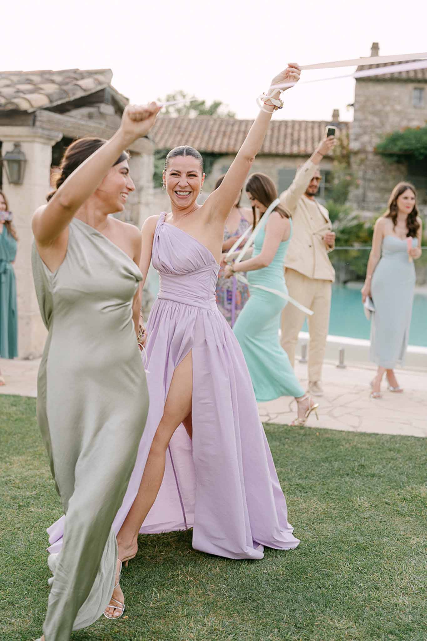 Guests pulling white ribbons on villa lawn with bridesmaids in coordinated sage and lavender dresses