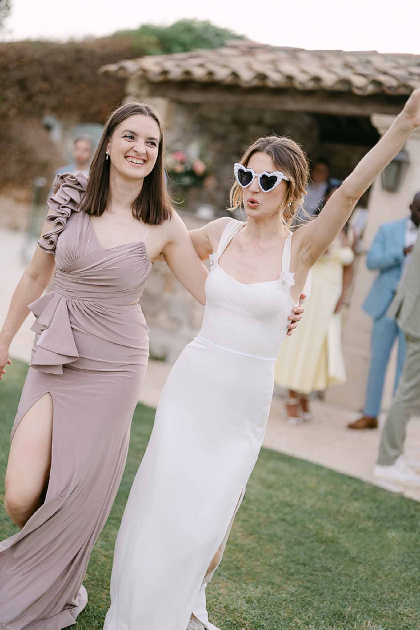 Bride in ivory gown and bridesmaid in mauve dress celebrating at outdoor reception in rustic stone courtyard