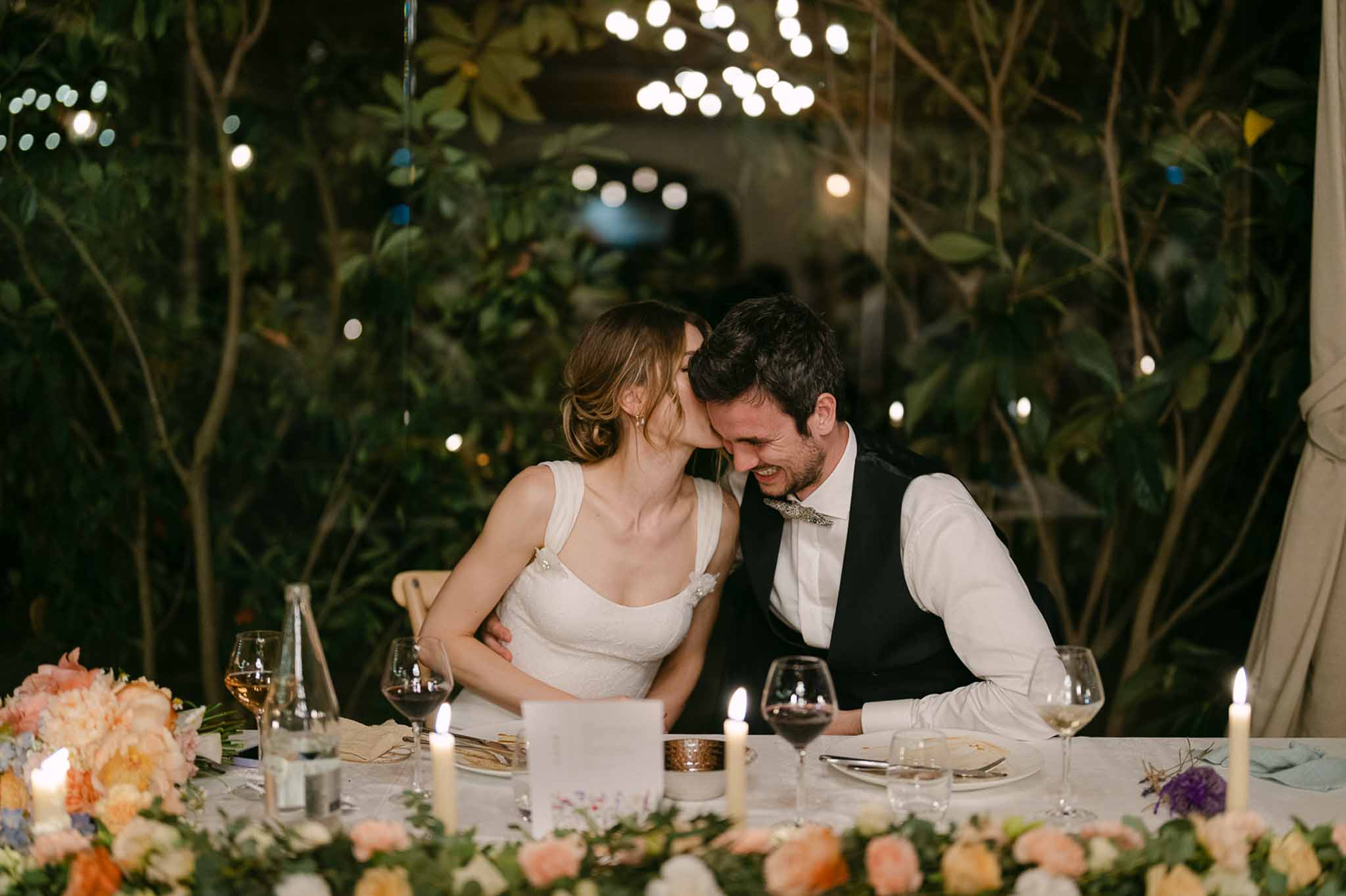Bride and groom at reception table with coral carnation centerpieces and globe string lights