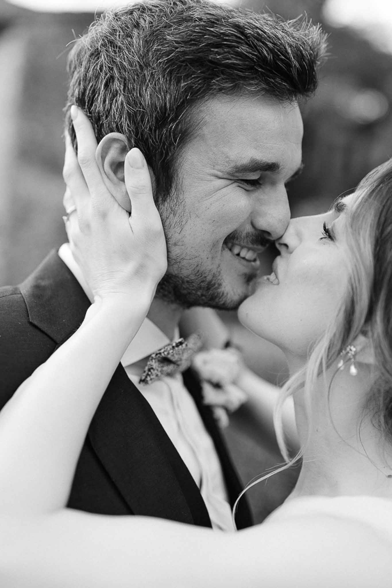 Black and white close-up of bride kissing groom's cheek, his eyes closed, hands cradling his face