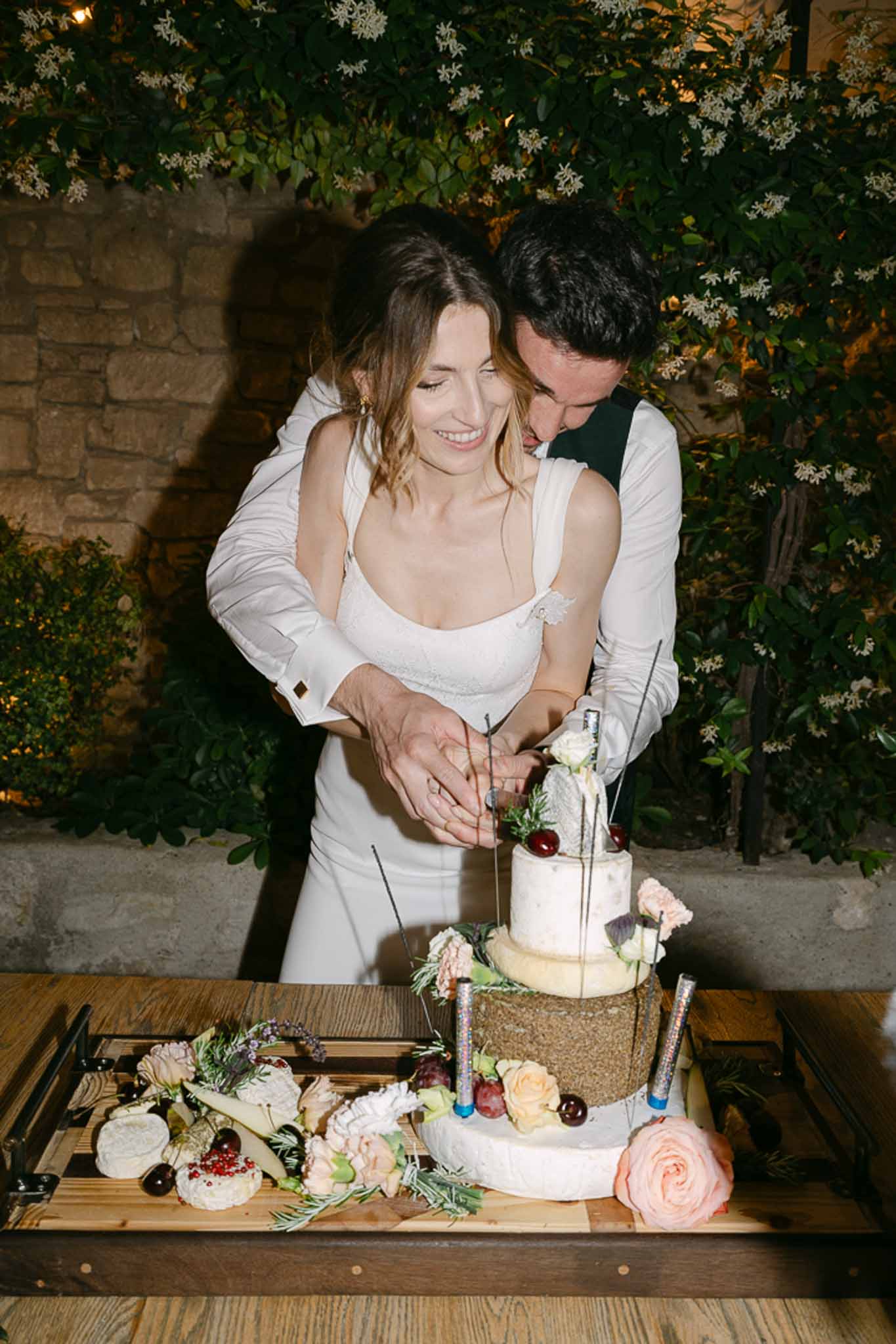 Bride and groom cutting a three-tiered cake with white and gold tiers decorated with peach roses and burgundy berries.