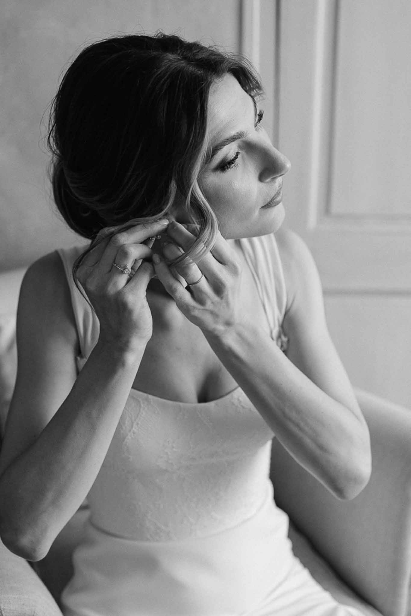 Black and white profile portrait of bride fastening a delicate necklace during getting-ready preparations