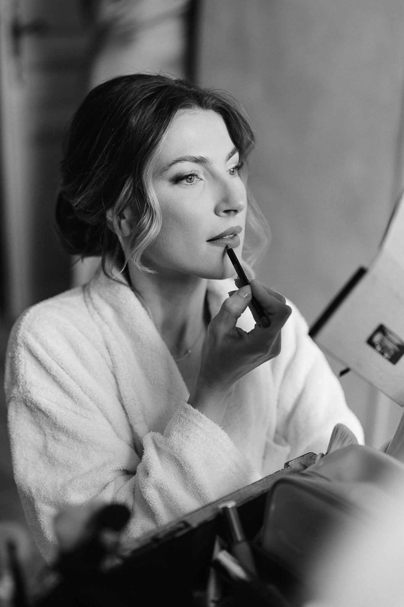 Bride applying lipstick while looking in a mirror during preparations