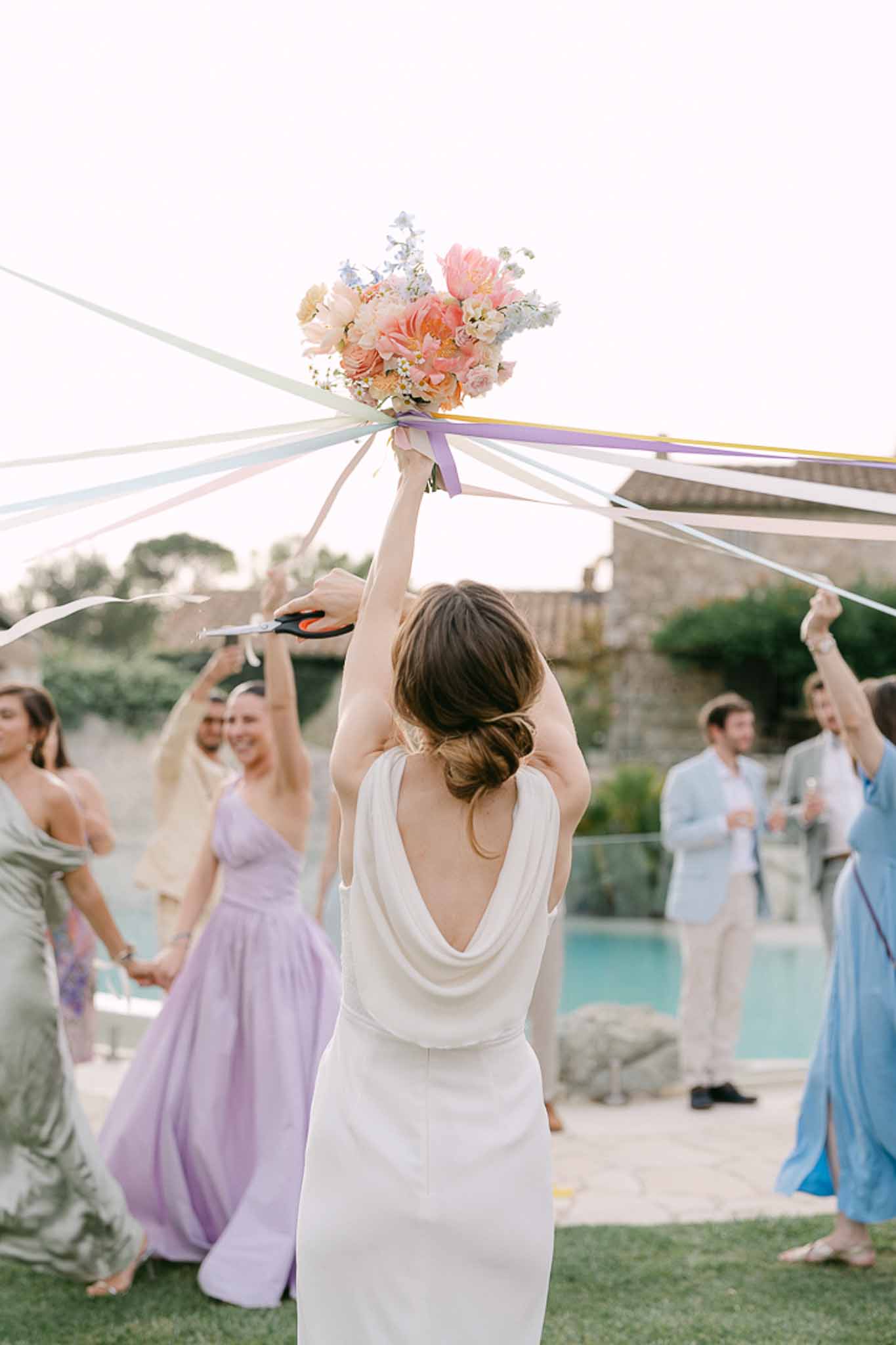 Bride tossing bouquet at poolside reception with bridesmaids in lavender and sage dresses