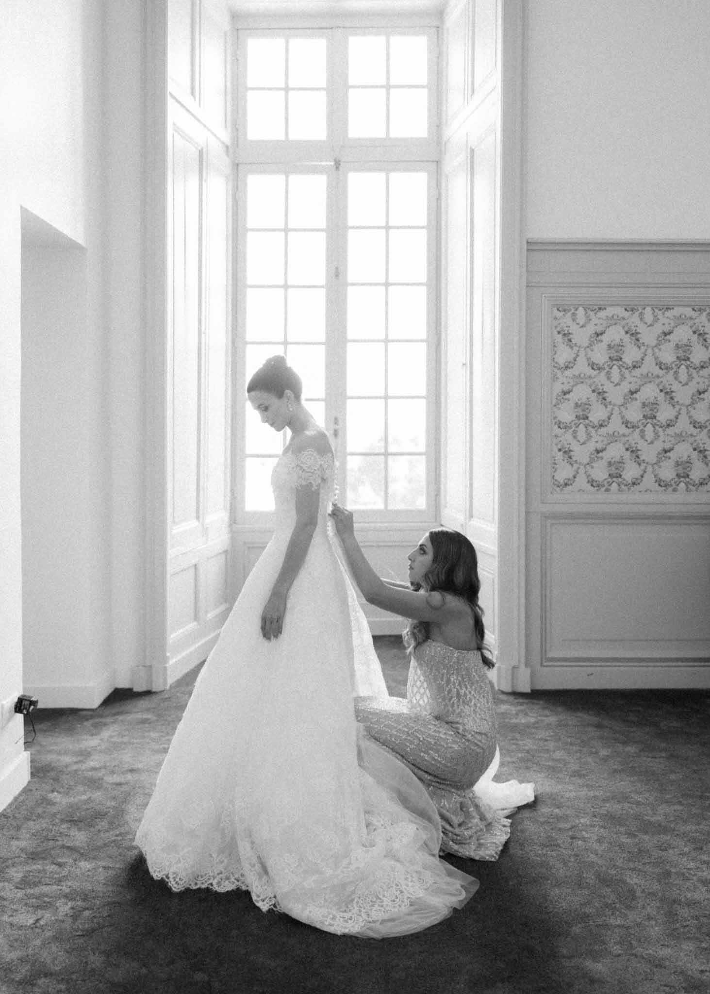 Black-and-white attendant adjusting bride's lace train in classical interior