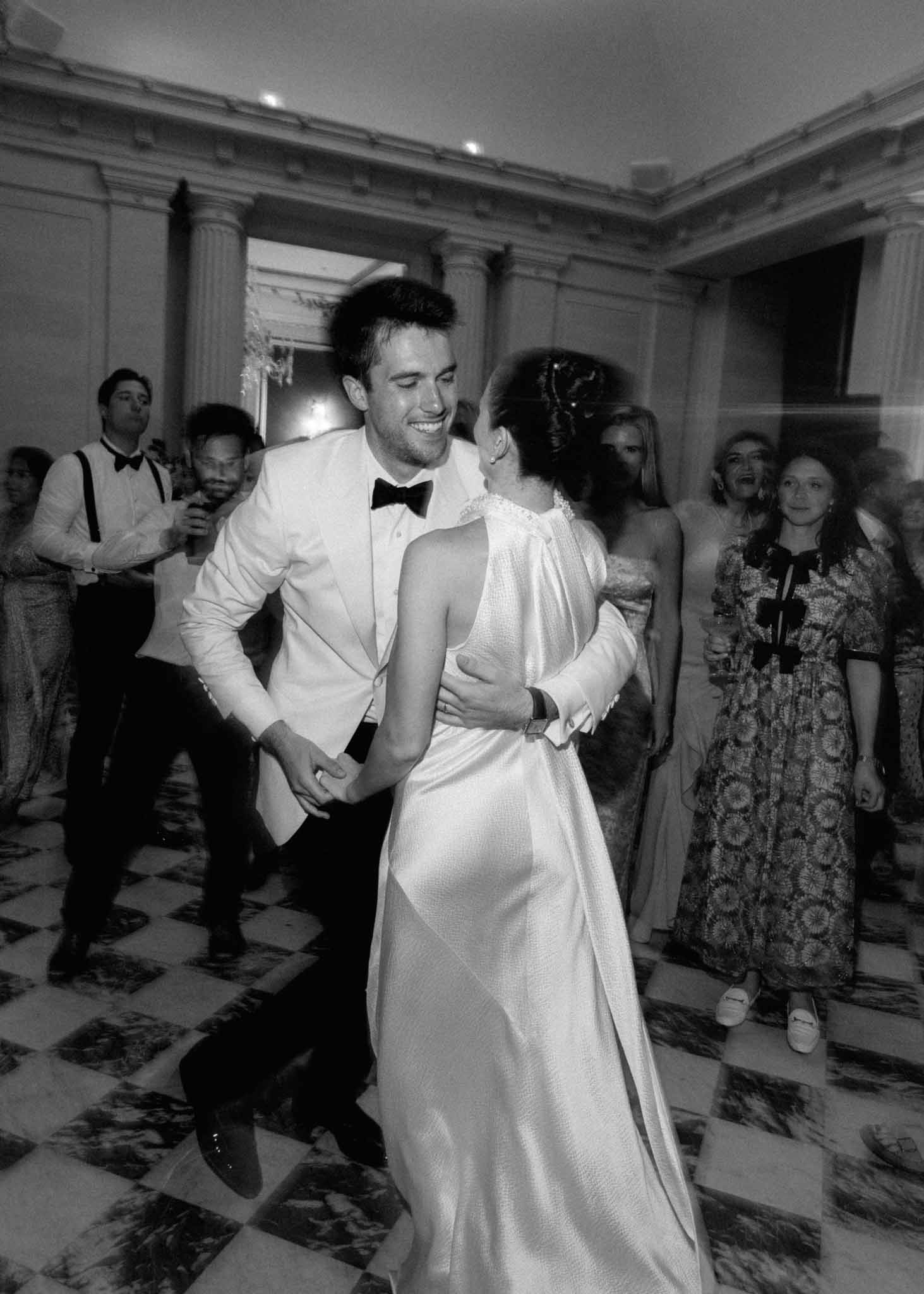 Black-and-white first dance in neoclassical ballroom with fluted columns and patterned floor