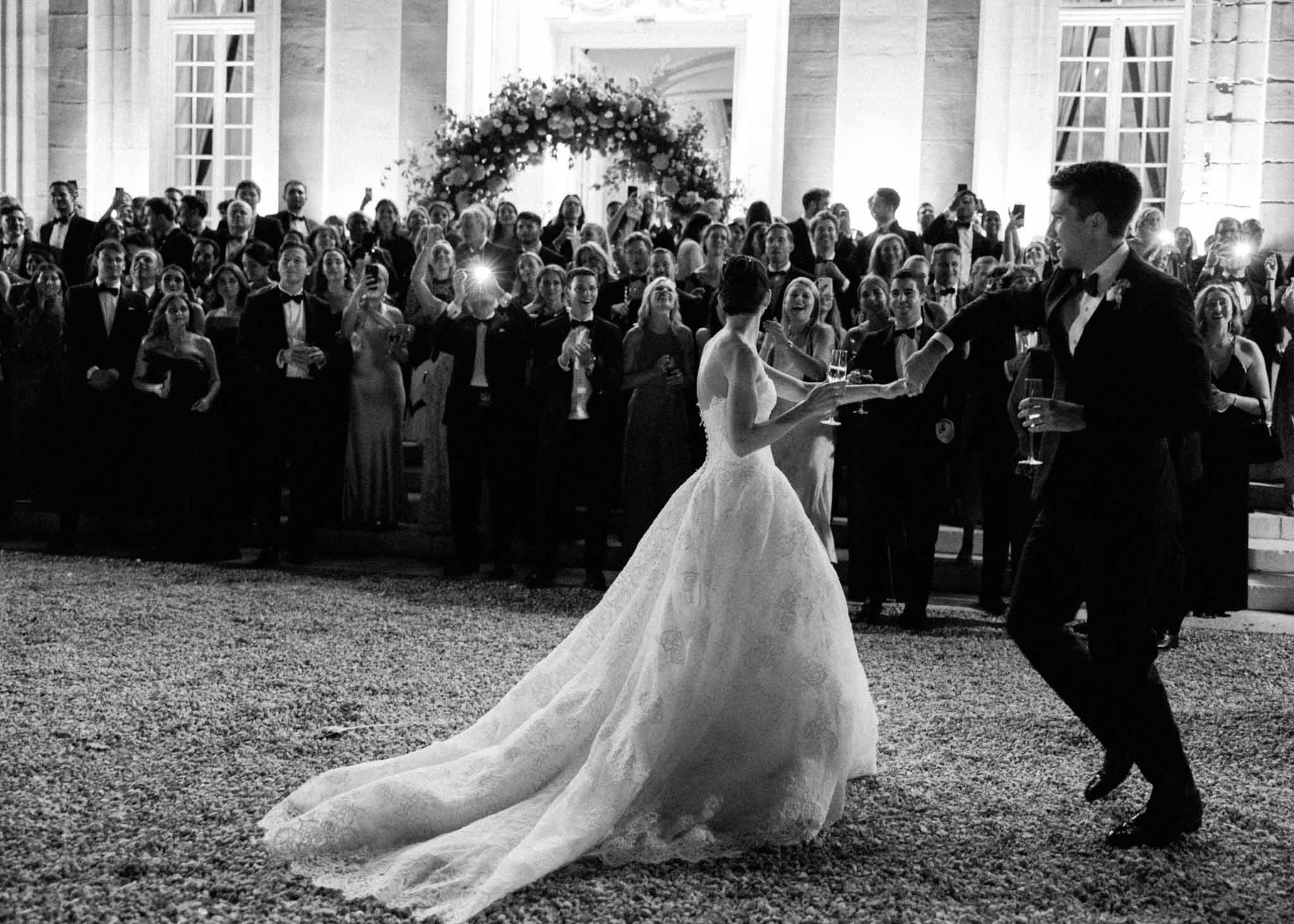 Bride and groom first dance in outdoor courtyard of neoclassical venue with 100 guests, black and white photo